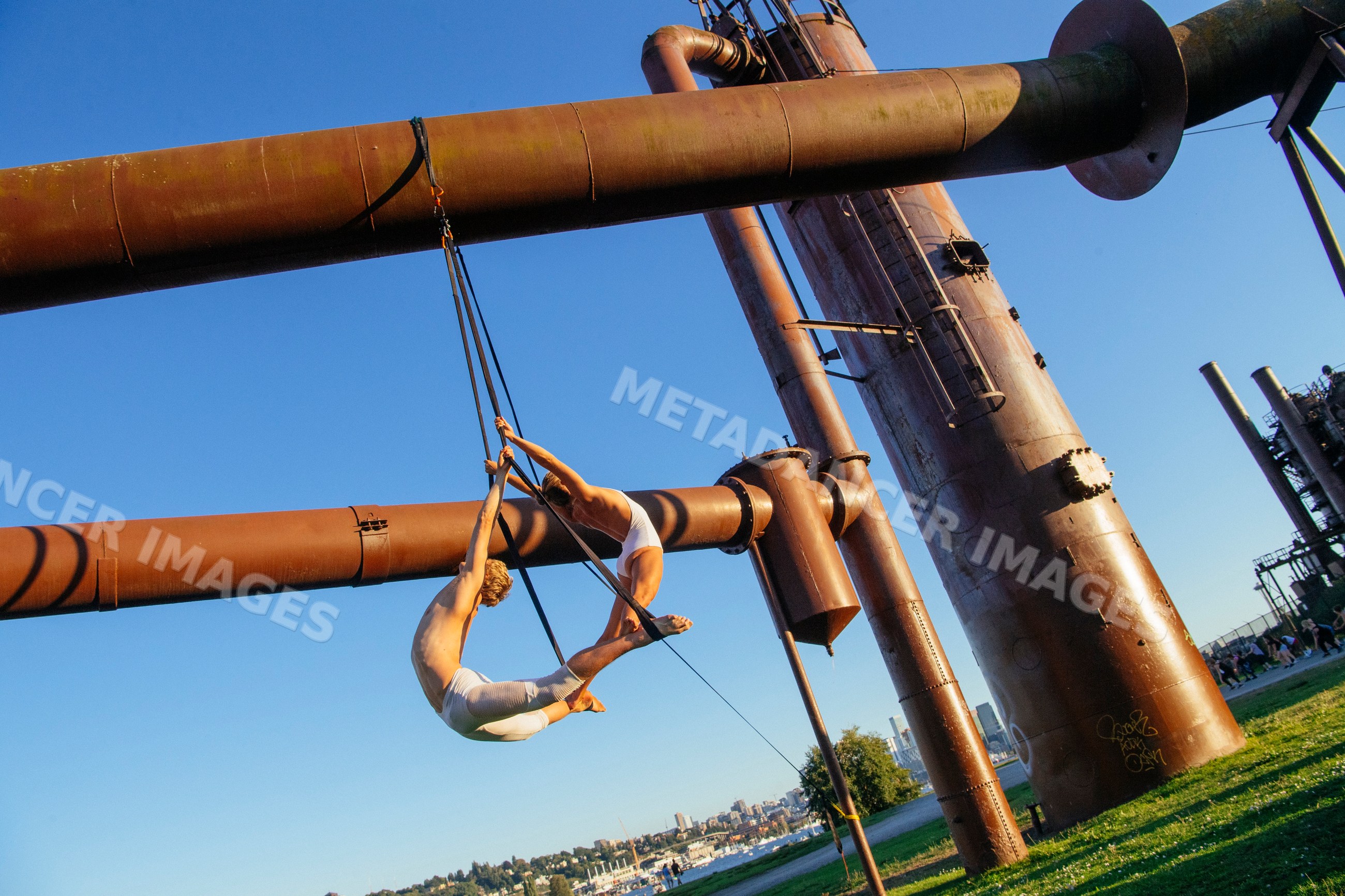 Two aerialists performing trapeze act on steel structure outdoors
