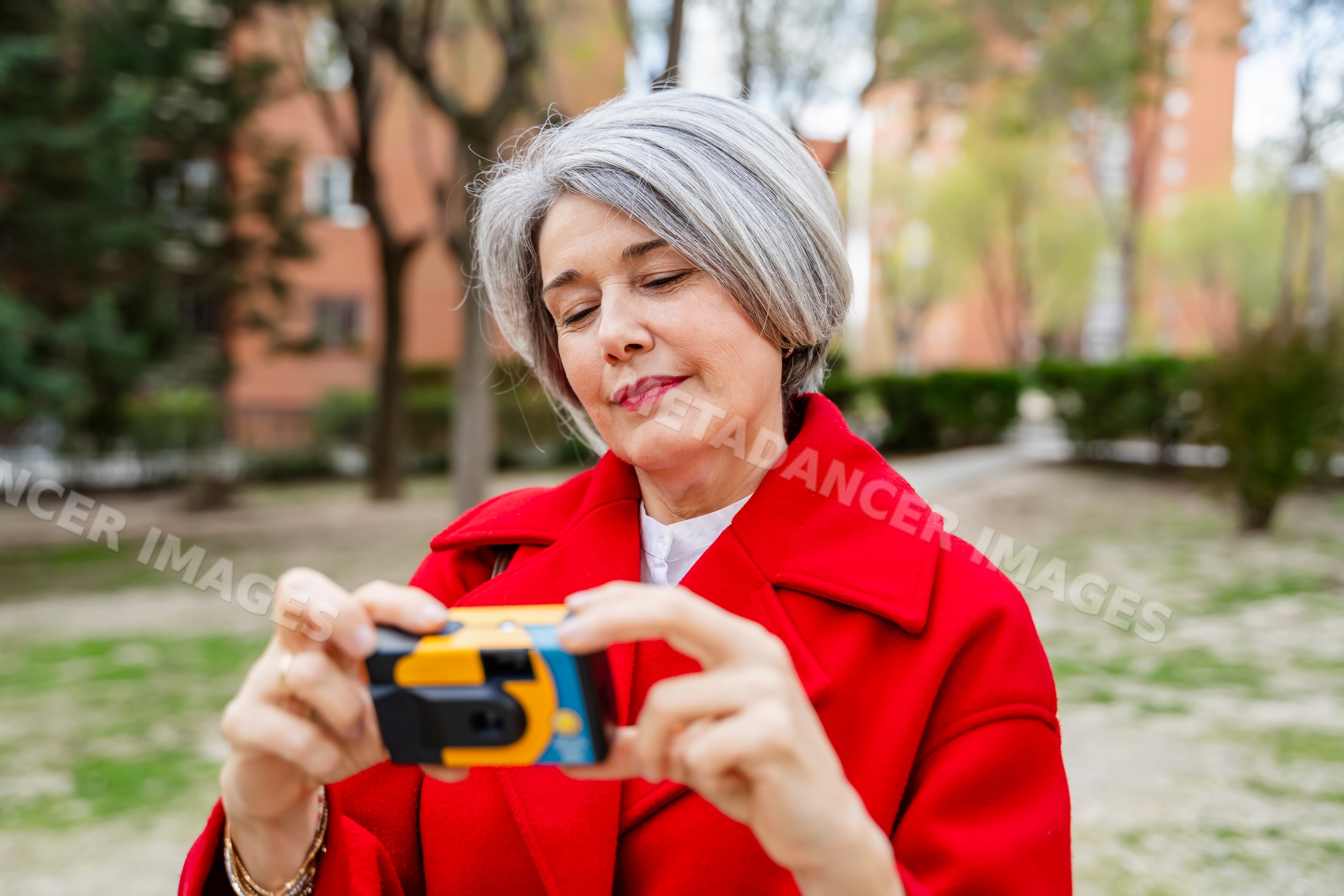White woman in red coat using camera outdoors