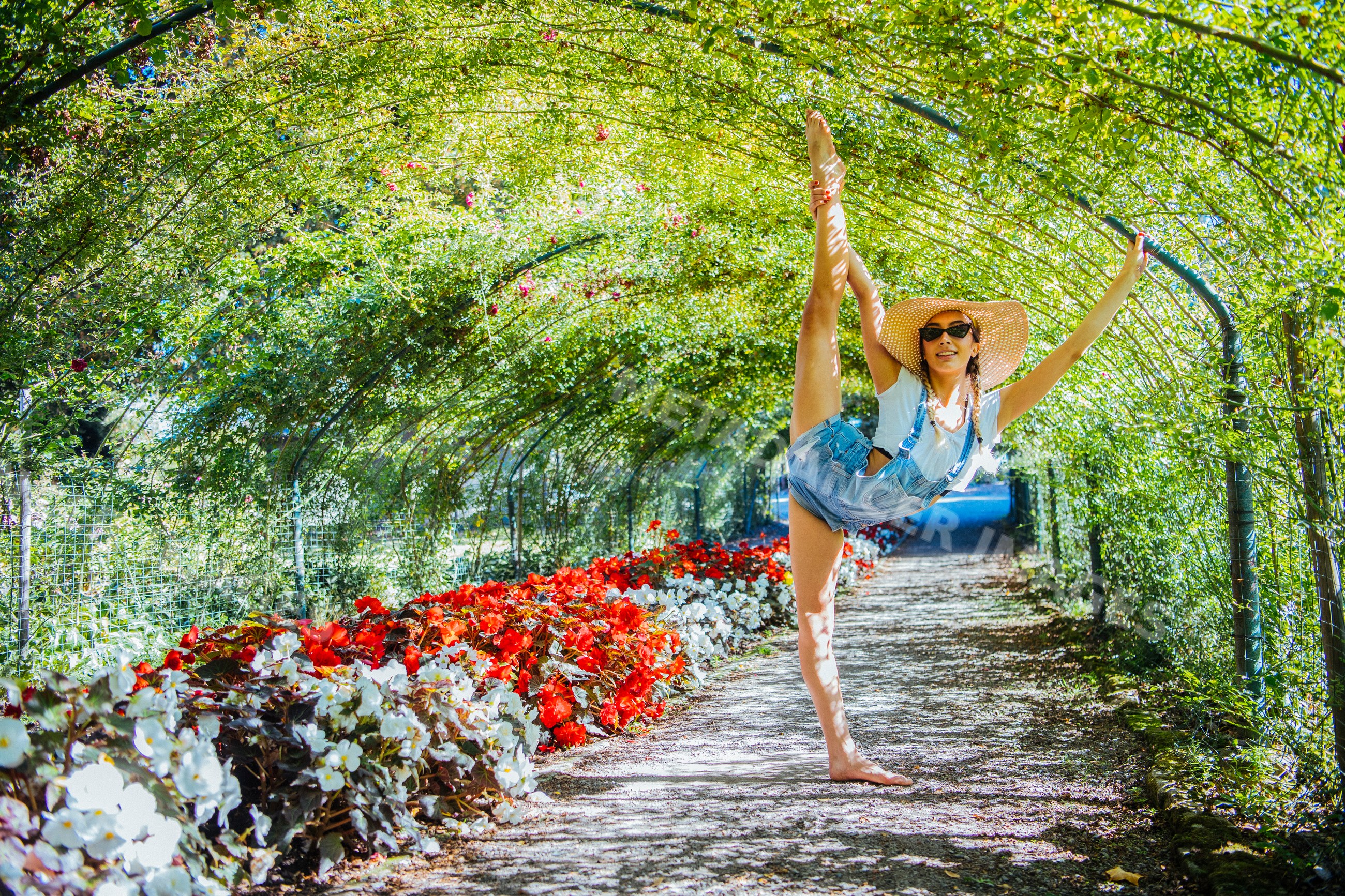 Contortionist stretching leg in flower-lined garden tunnel pathway
