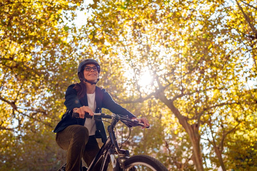 Hispanic woman cycling outdoors beneath autumn trees with sun flare