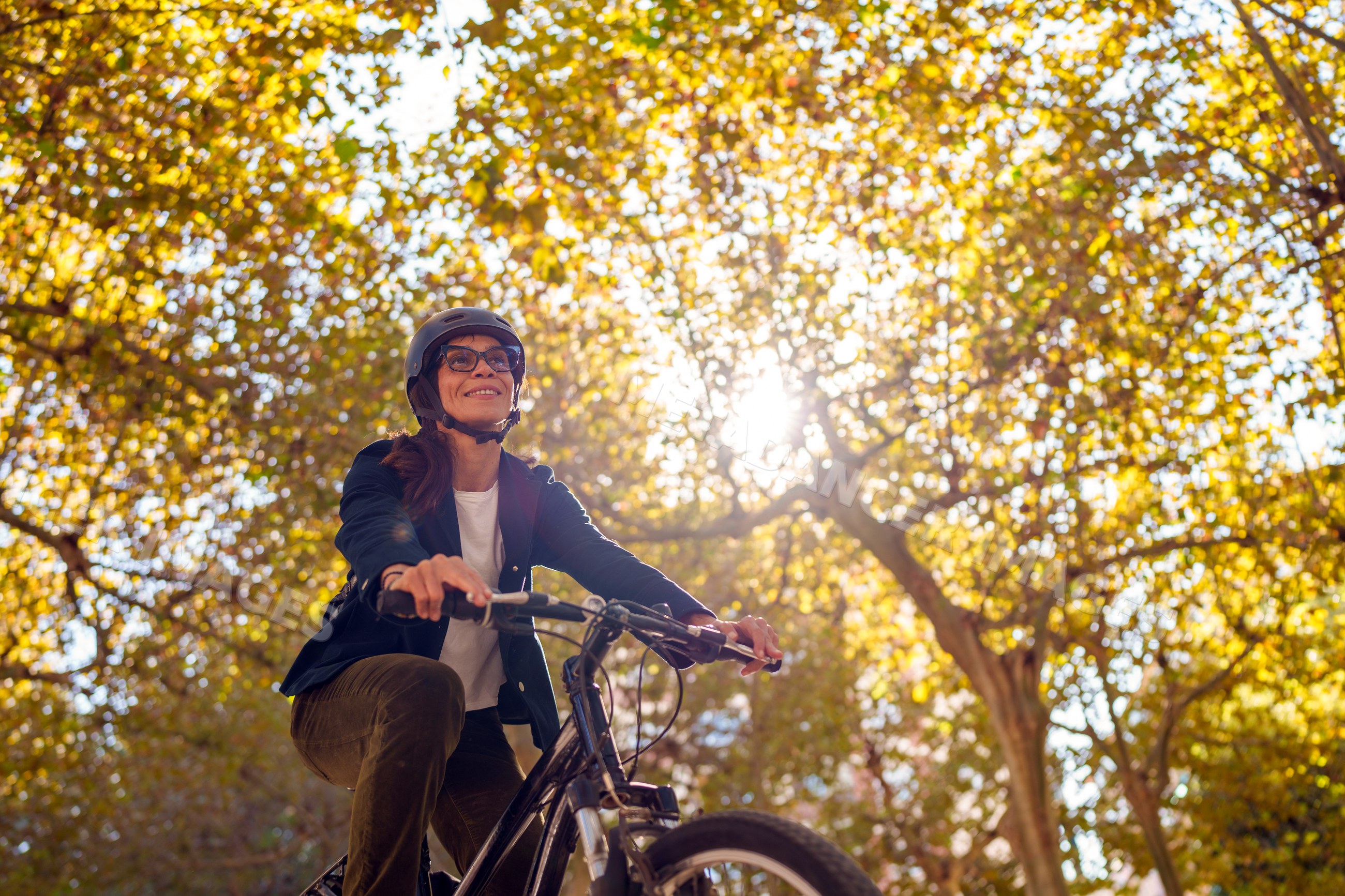 Hispanic woman cycling outdoors beneath autumn trees with sun flare