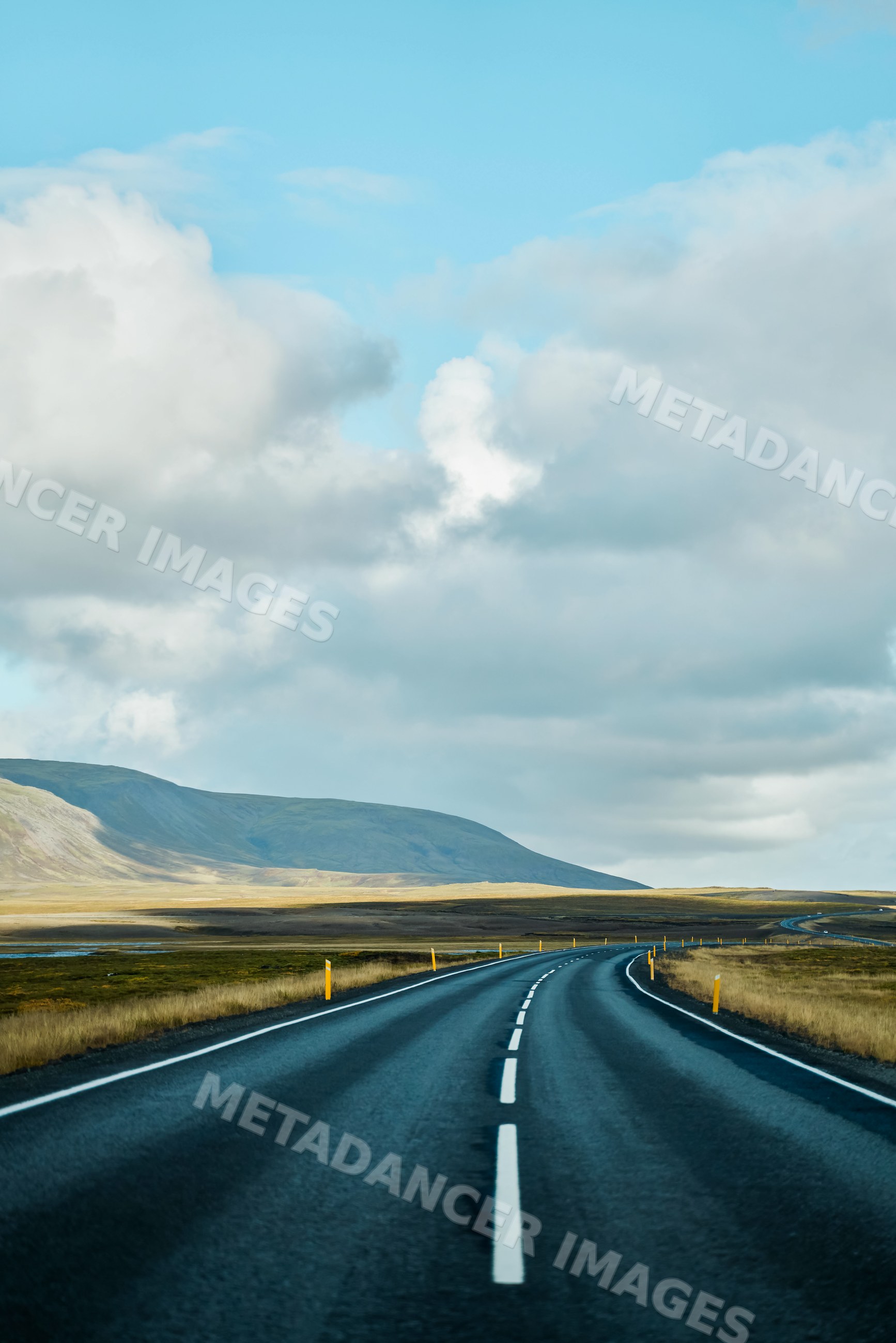 A winding empty asphalt road stretches across open grassland