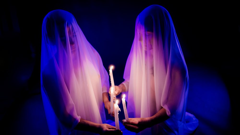 Two ghost figures holding candles in dark illuminated setting