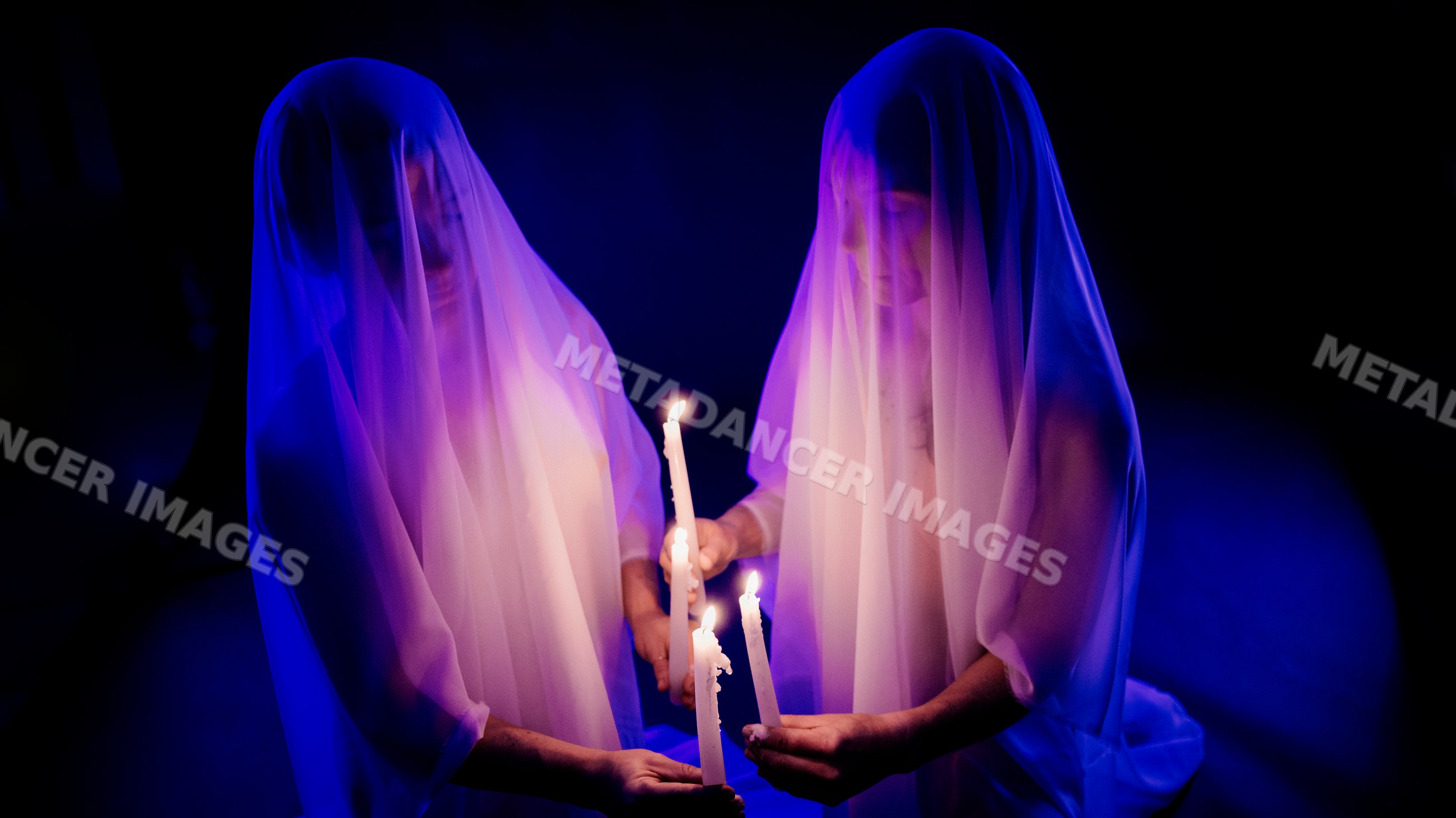 Two ghost figures holding candles in dark illuminated setting