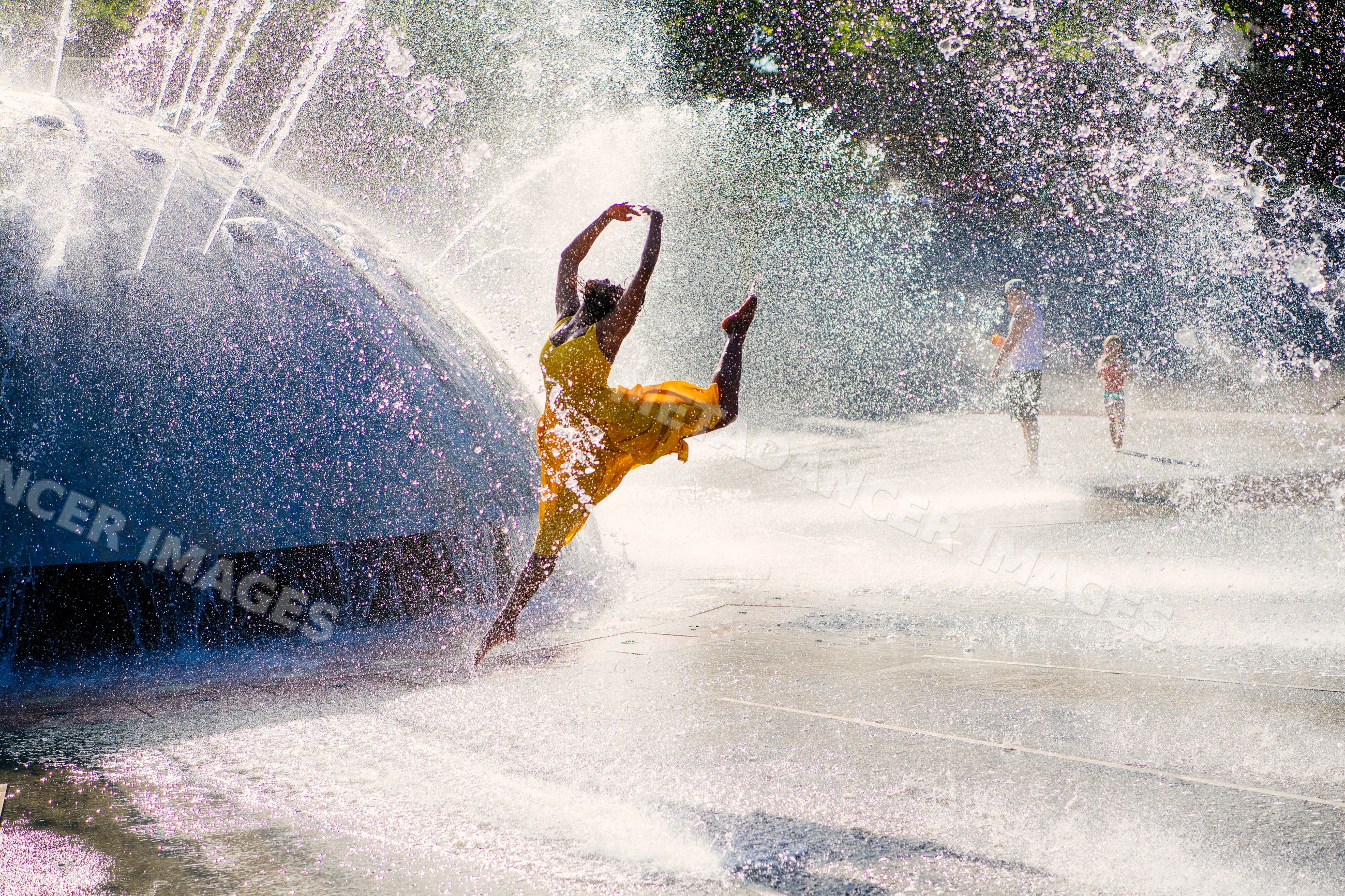 South Asian woman jumping and dancing by water fountain splashing