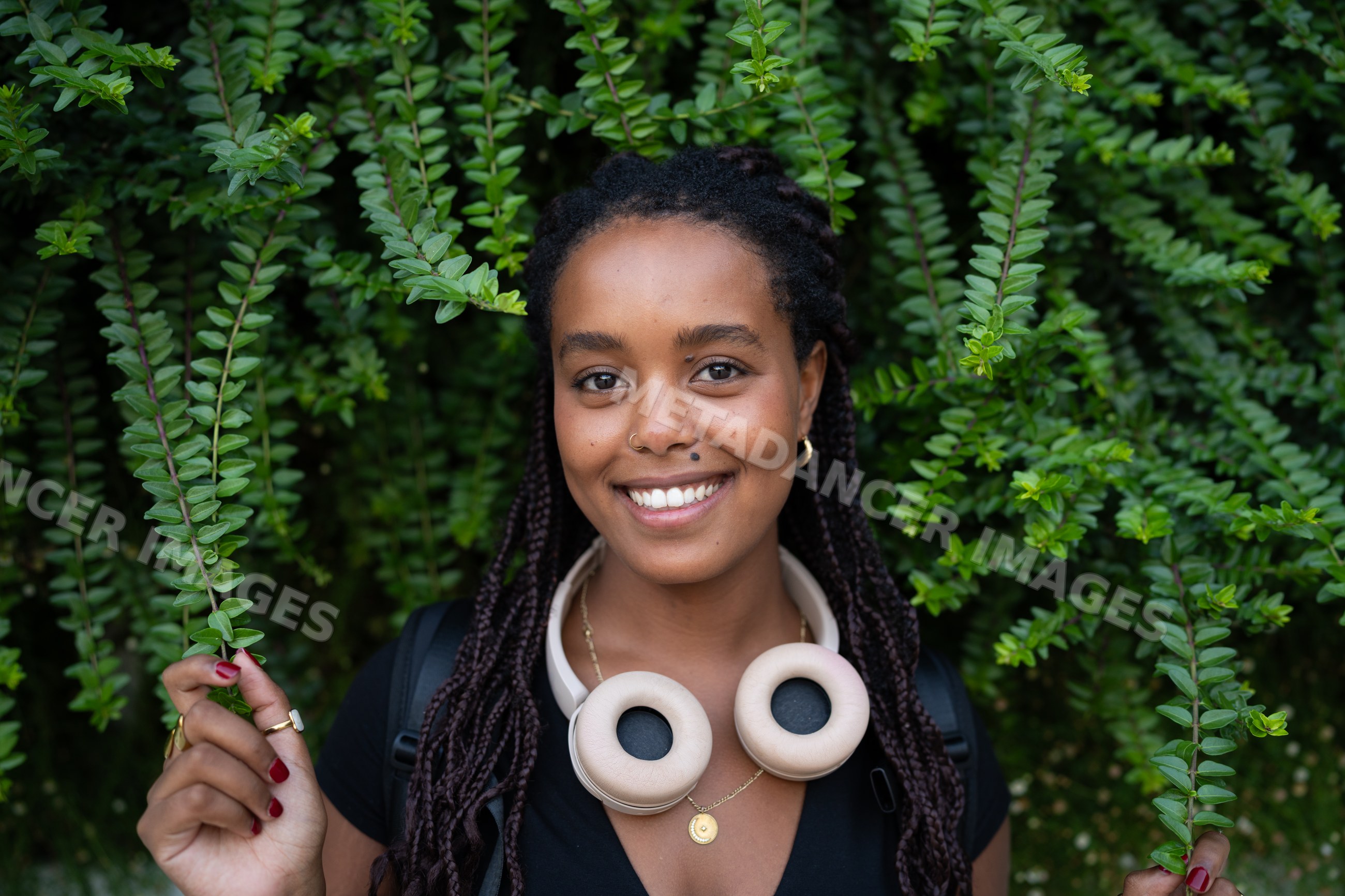 A smiling African American woman with headphones holds green leaves