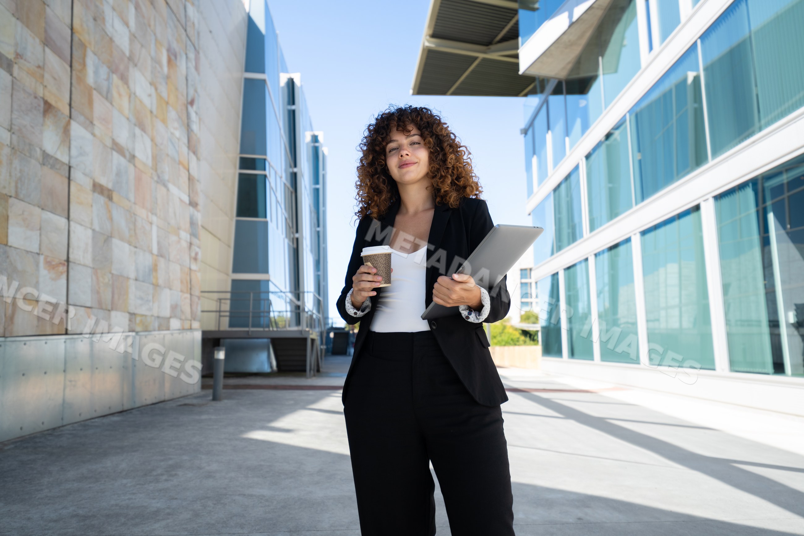 Businesswoman holding coffee and laptop outside modern office