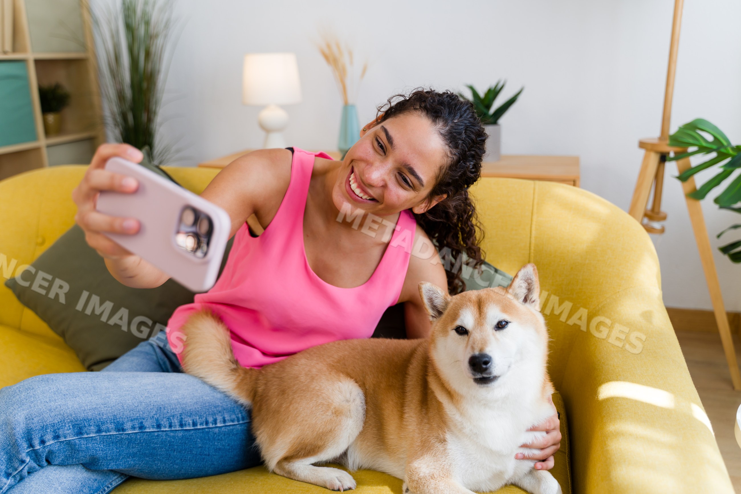 A Hispanic woman takes a selfie with her dog on a yellow couch