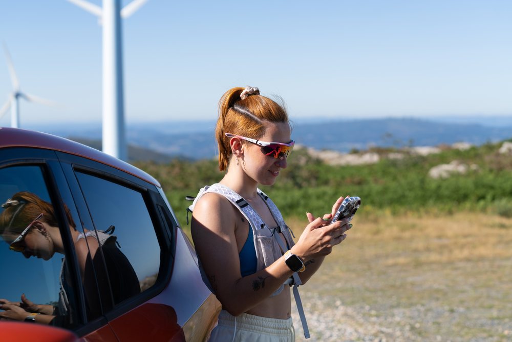 A white woman uses her smartphone beside a car with wind turbines