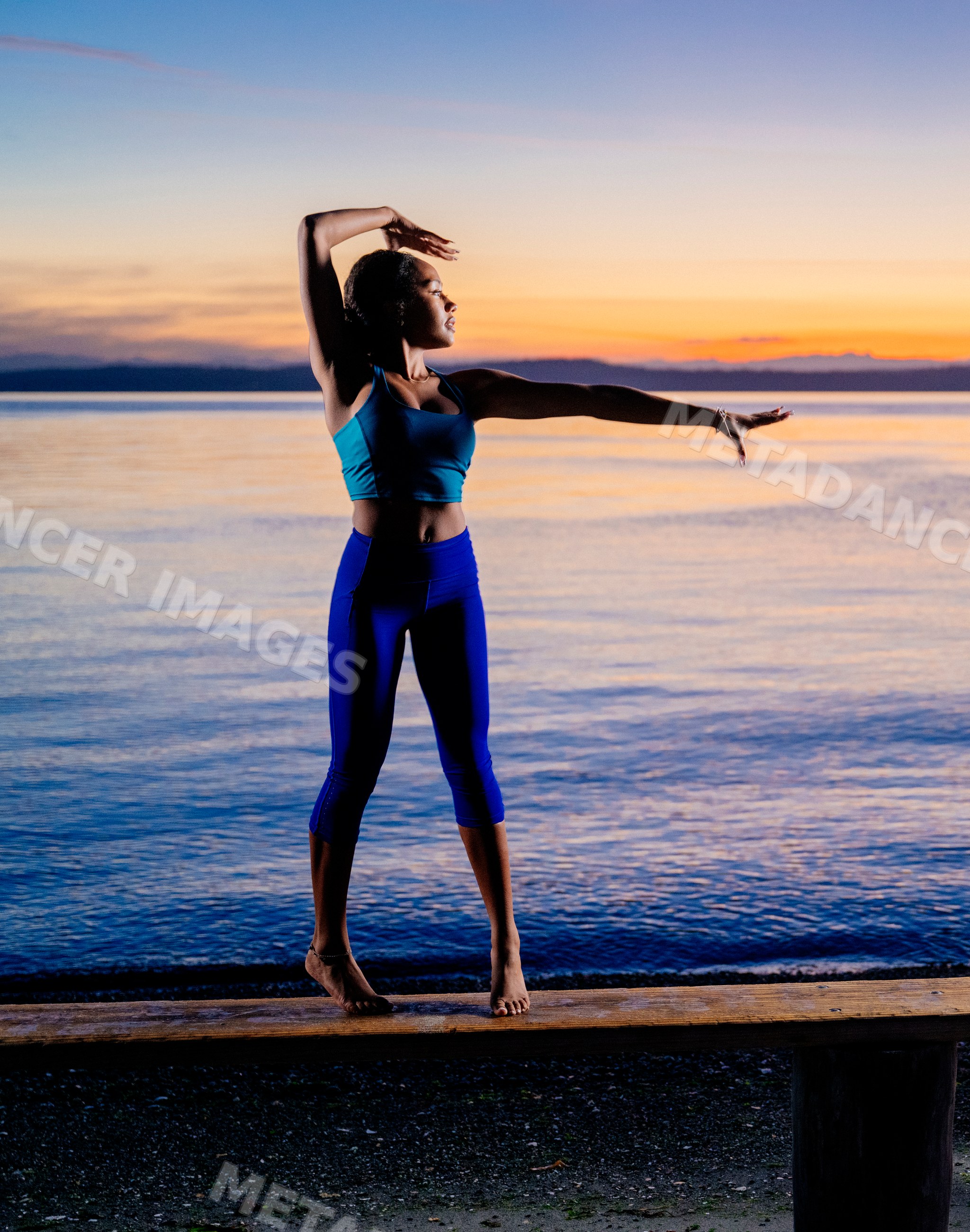 Hispanic woman stretching and balancing near lake at sunset in the USA