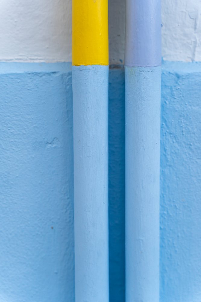 Close-up of painted yellow and blue pipes on blue textured wall