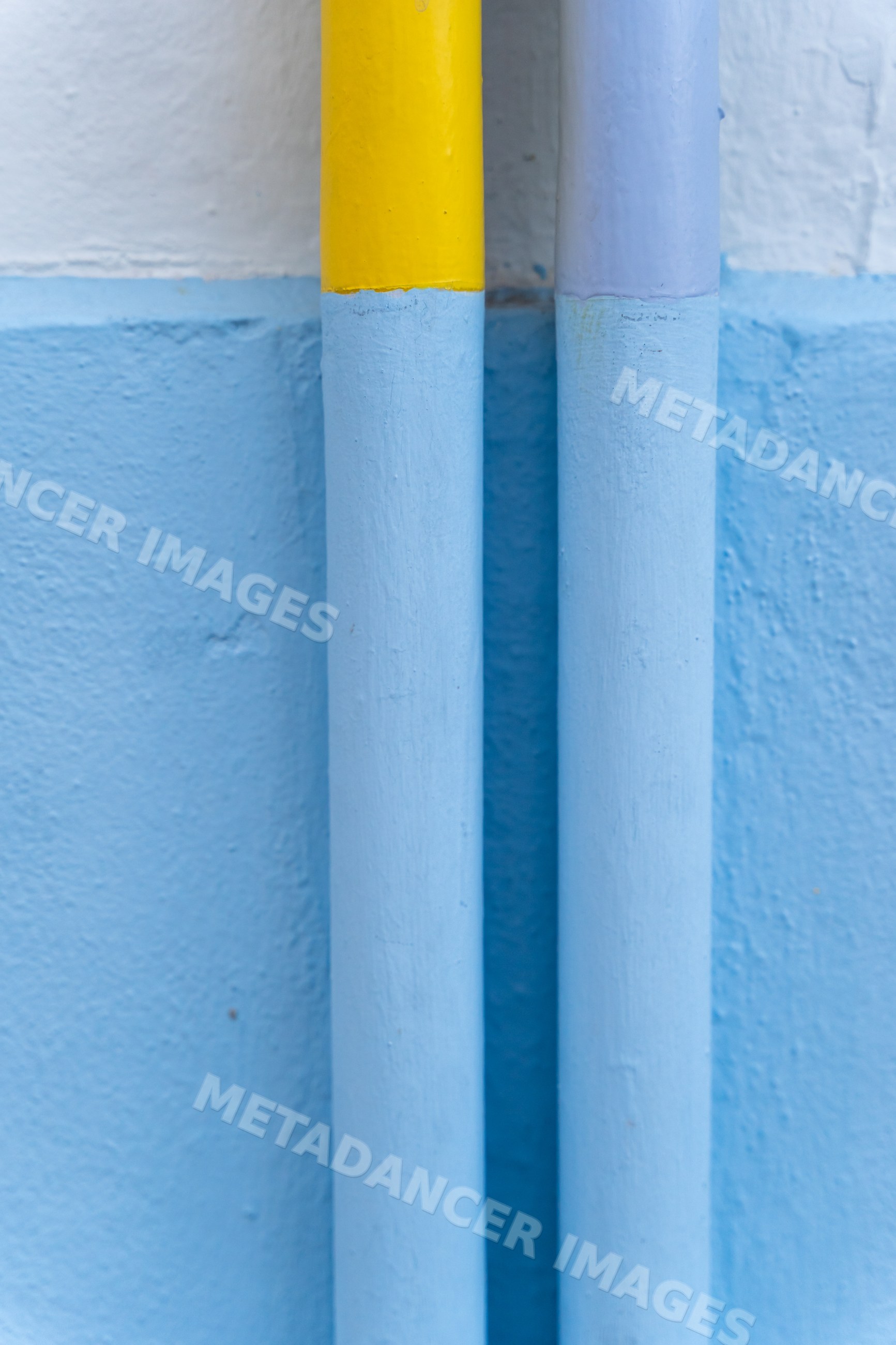 Close-up of painted yellow and blue pipes on blue textured wall