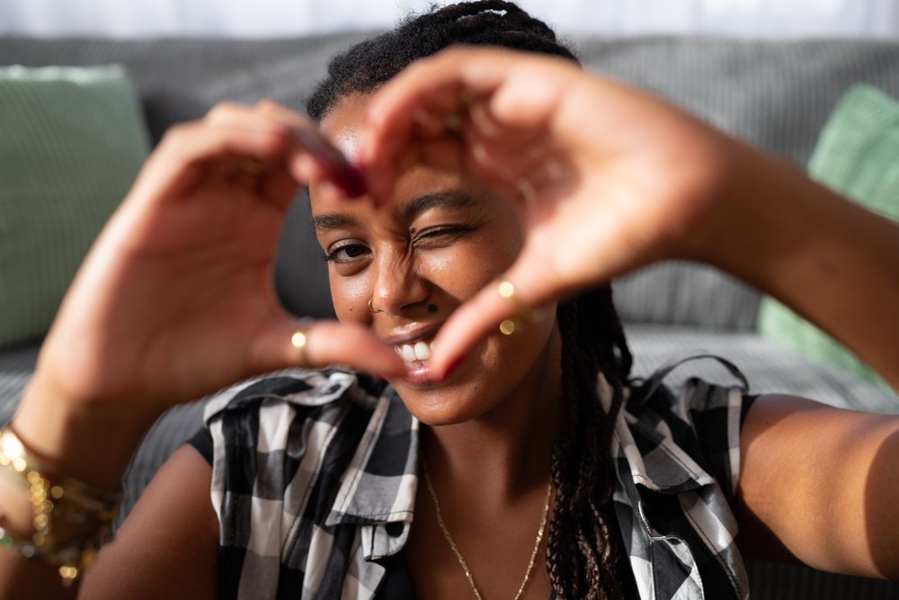 A young African American woman makes a heart shape with her hands