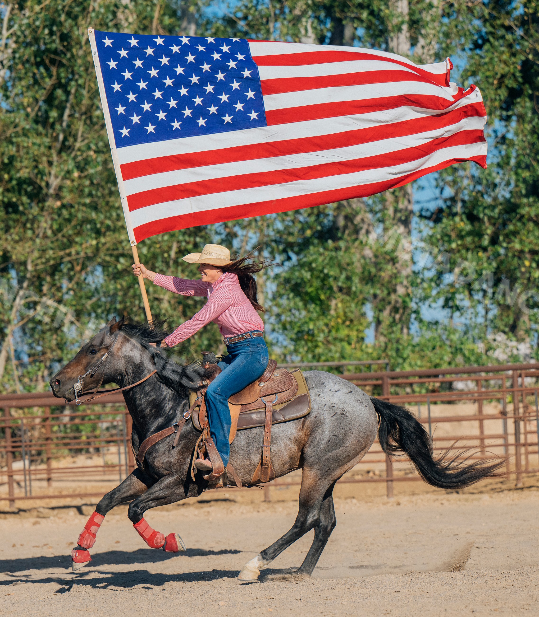 White woman riding horse holding large american flag in rodeo arena