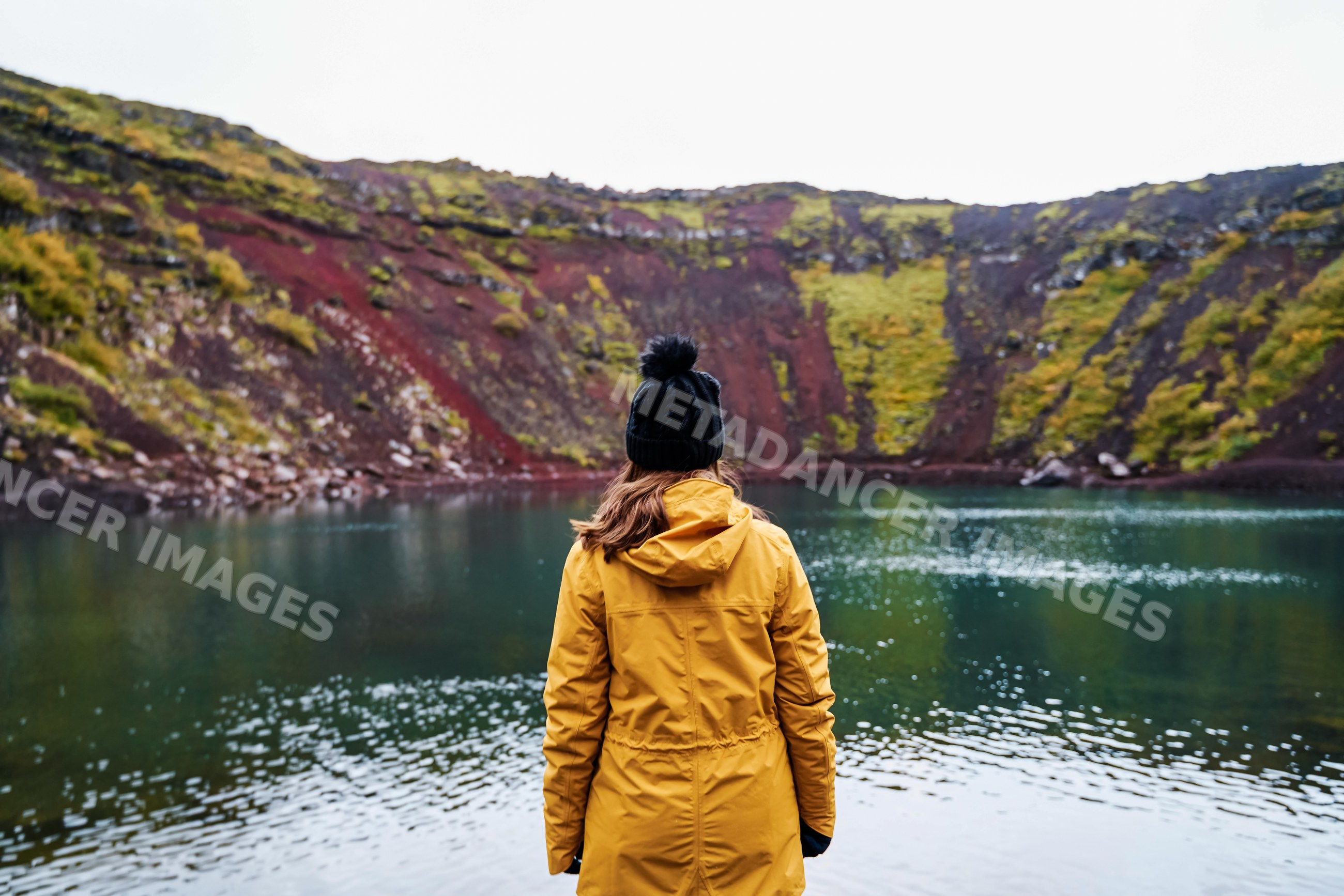 A white woman in a yellow jacket stands by a volcanic crater lake