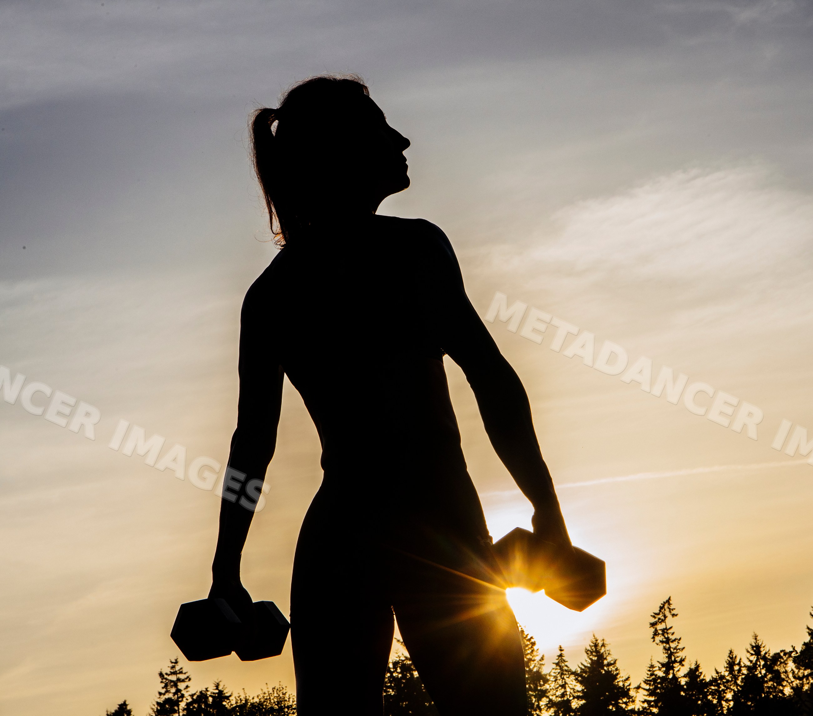 White woman lifting dumbbells outdoors during sunset