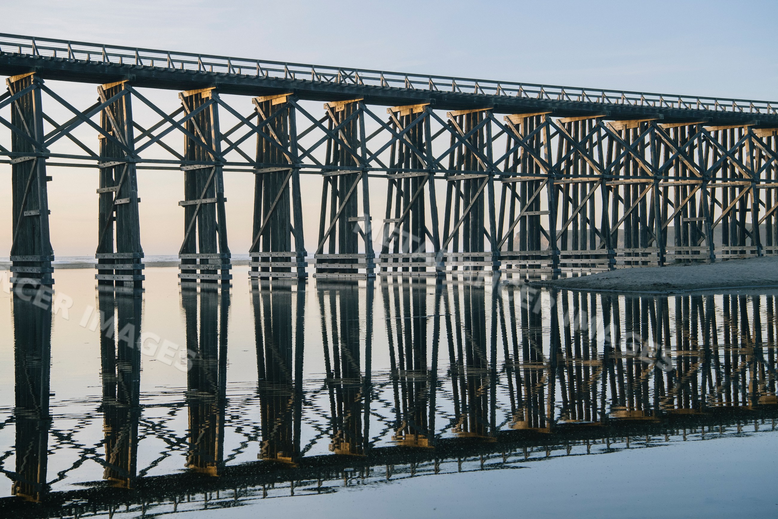 Wooden bridge reflecting in calm coastal waters at sunset
