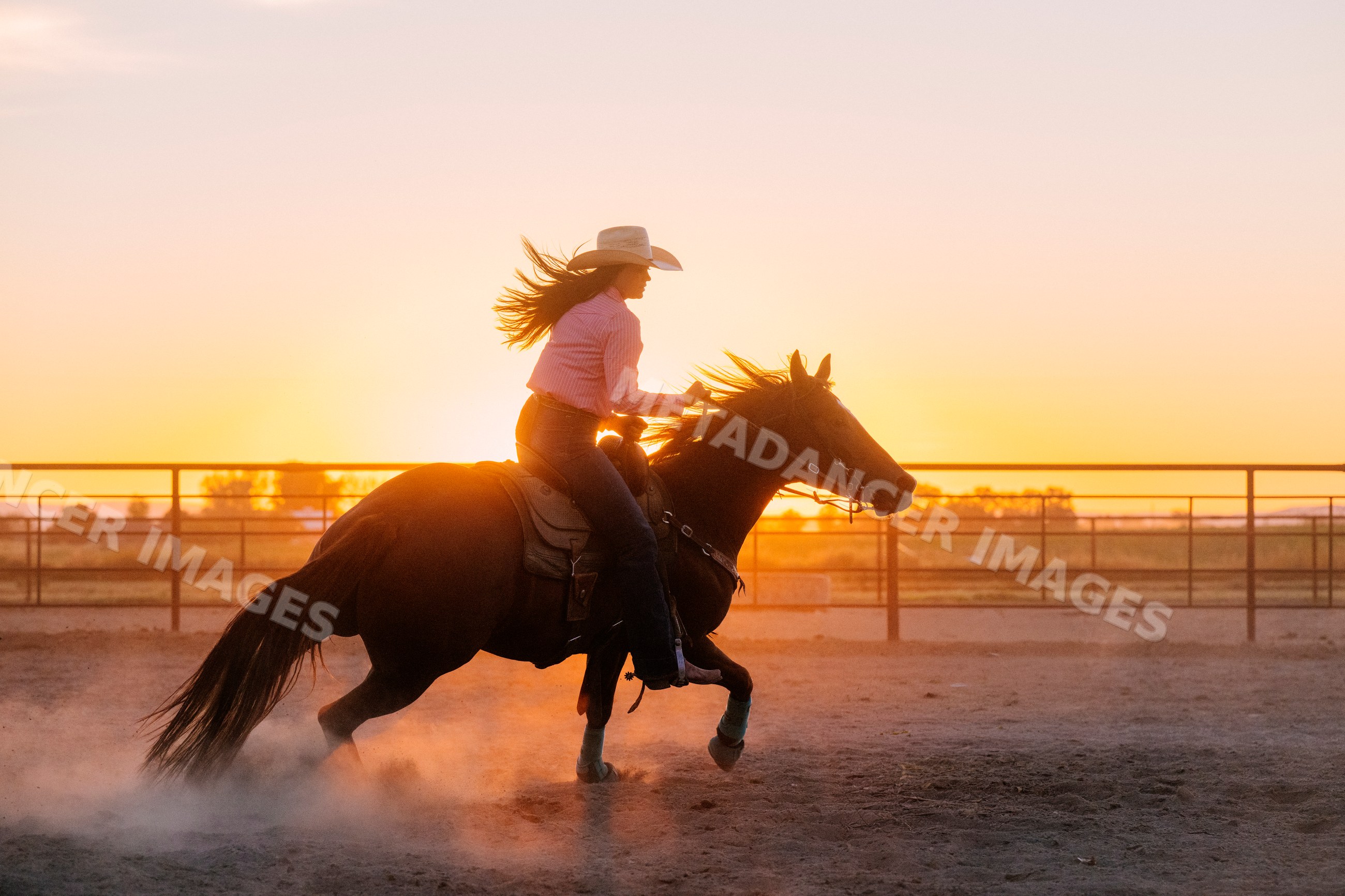 Cowgirl riding horse in dusty arena at sunset in Southwest USA