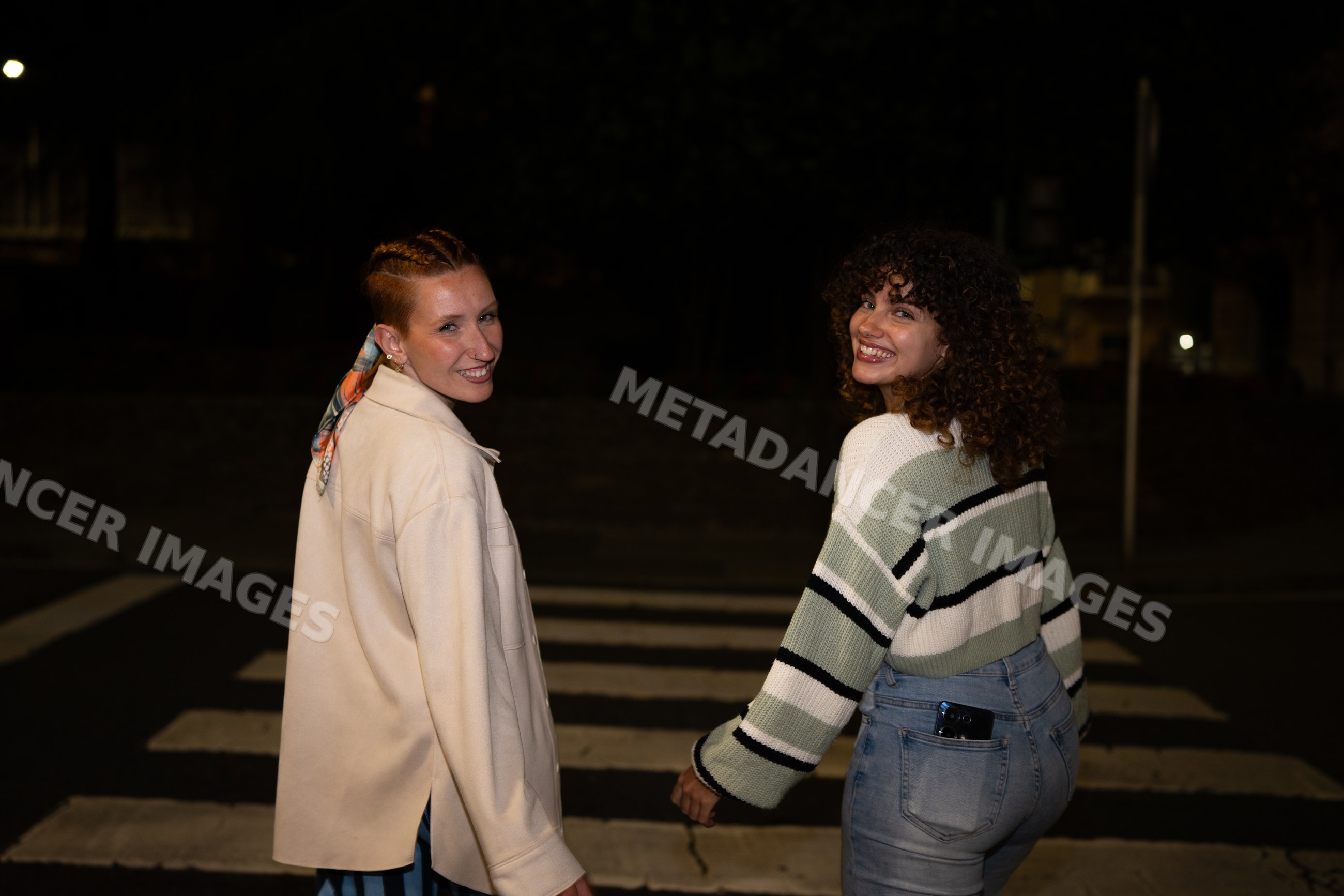 Two white women smiling while walking across crosswalk at night