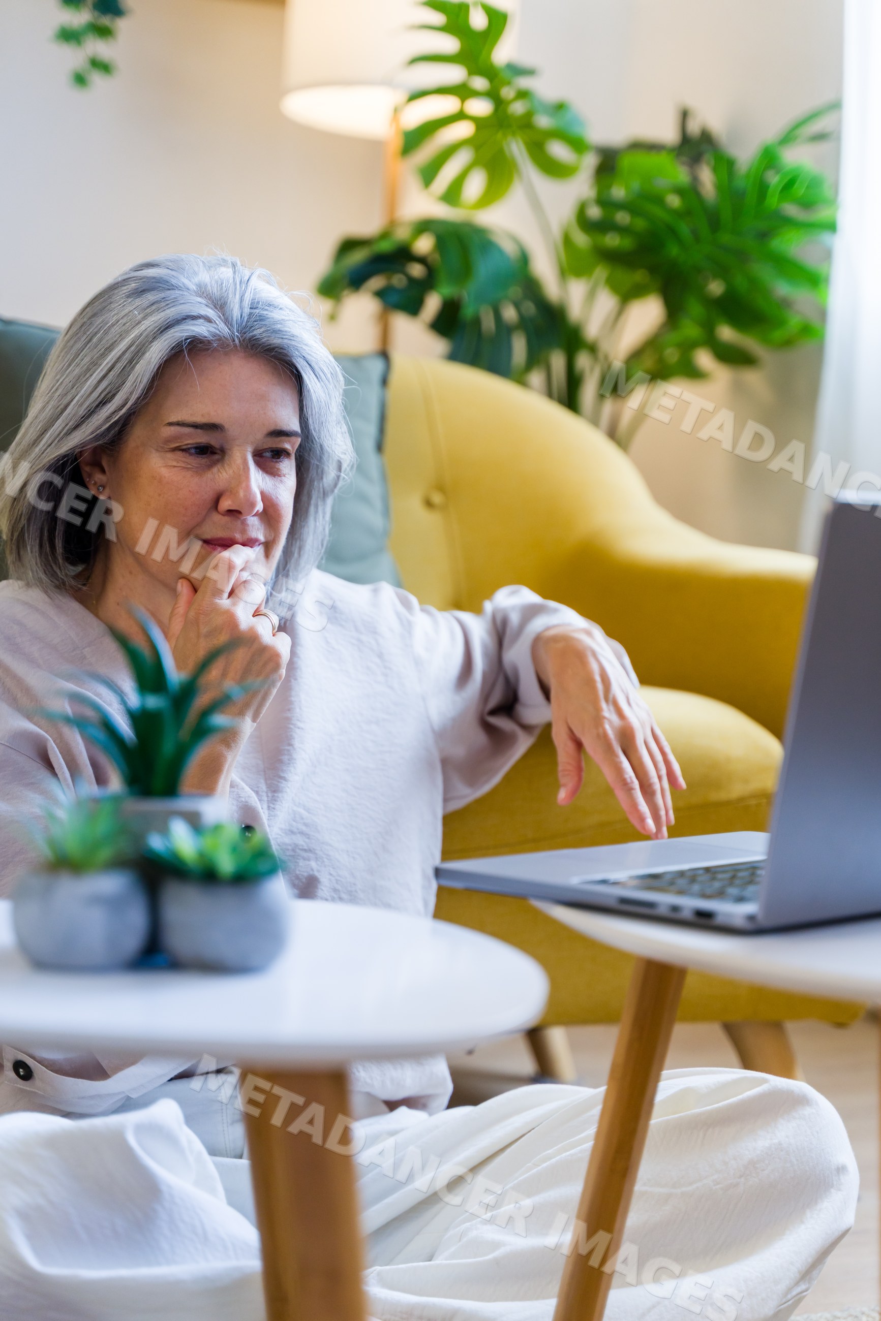 White woman using laptop in modern living room with yellow armchair