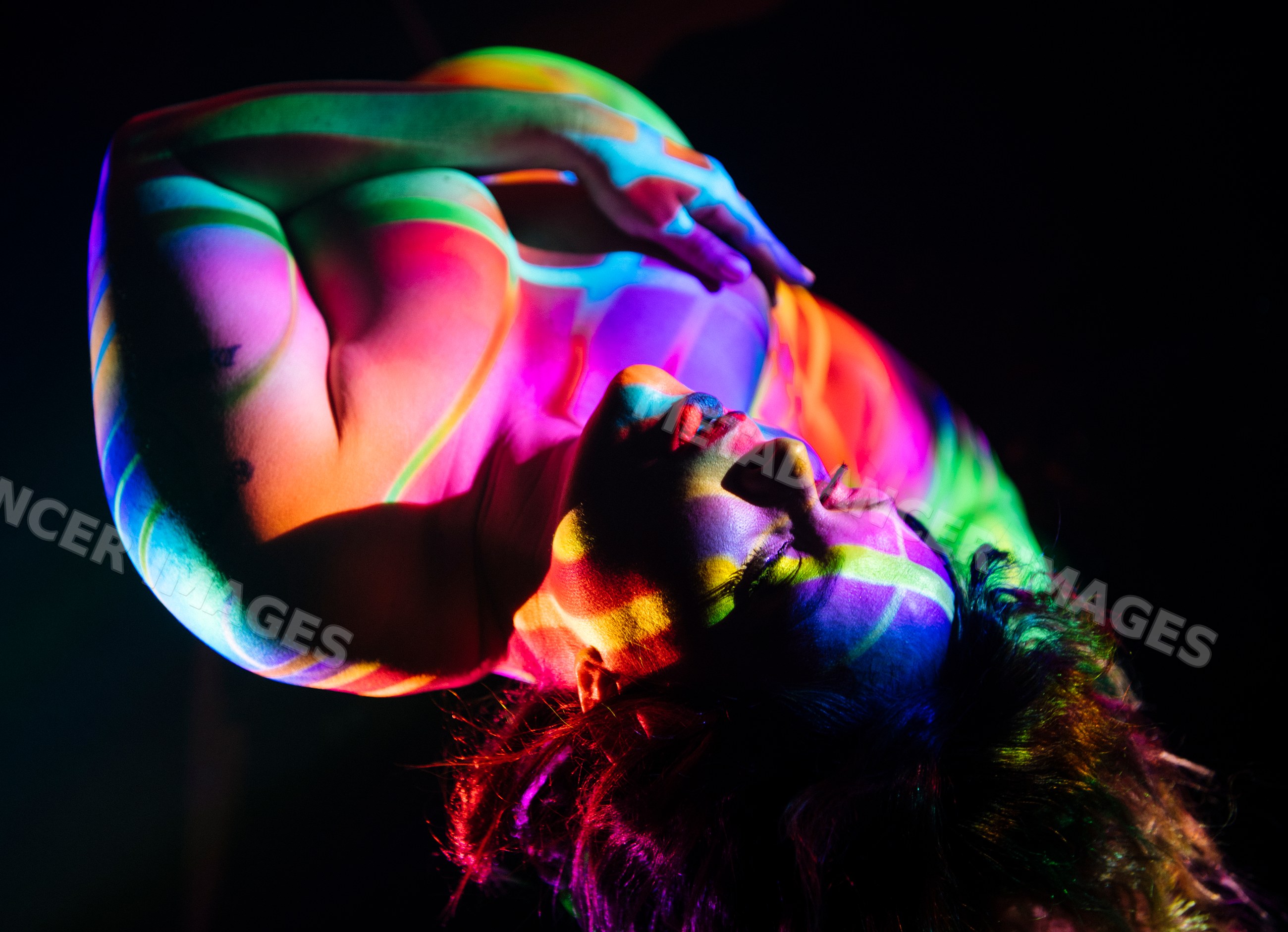White person posing with rainbow body painting under colorful light