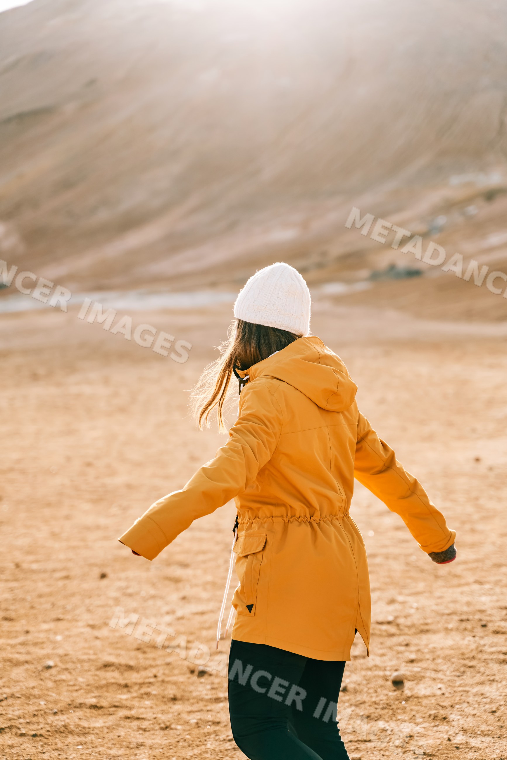 A white woman in a yellow jacket turns around on a dry landscape