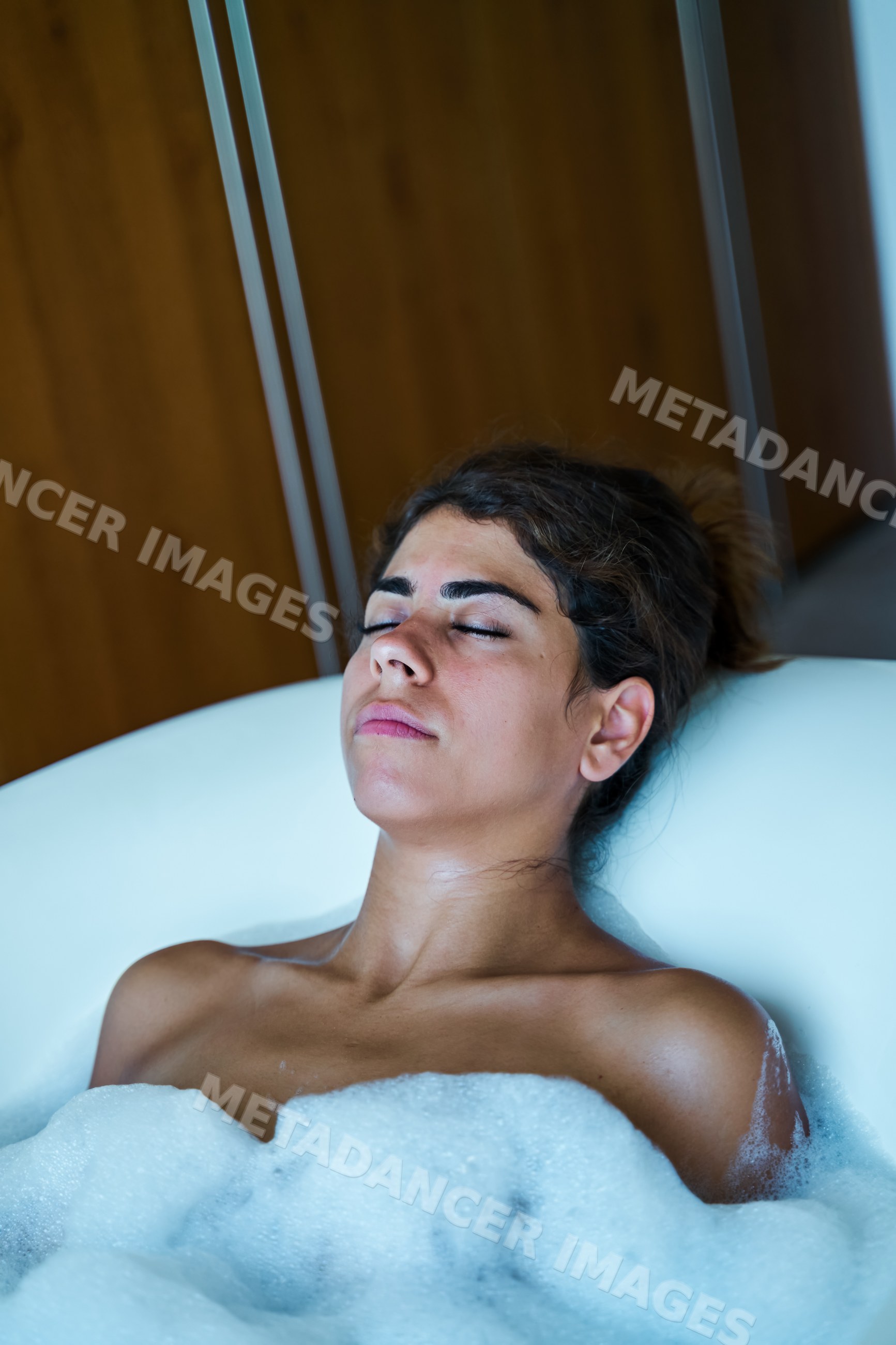 A white woman enjoys relaxing in a bubble bath with closed eyes