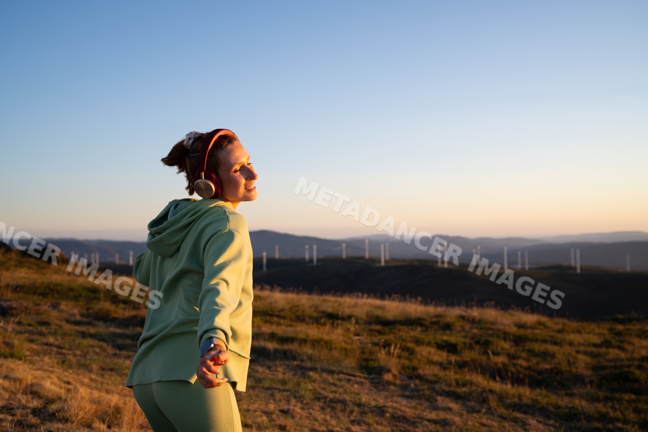 A white woman enjoys music outdoors near wind turbines in Galicia