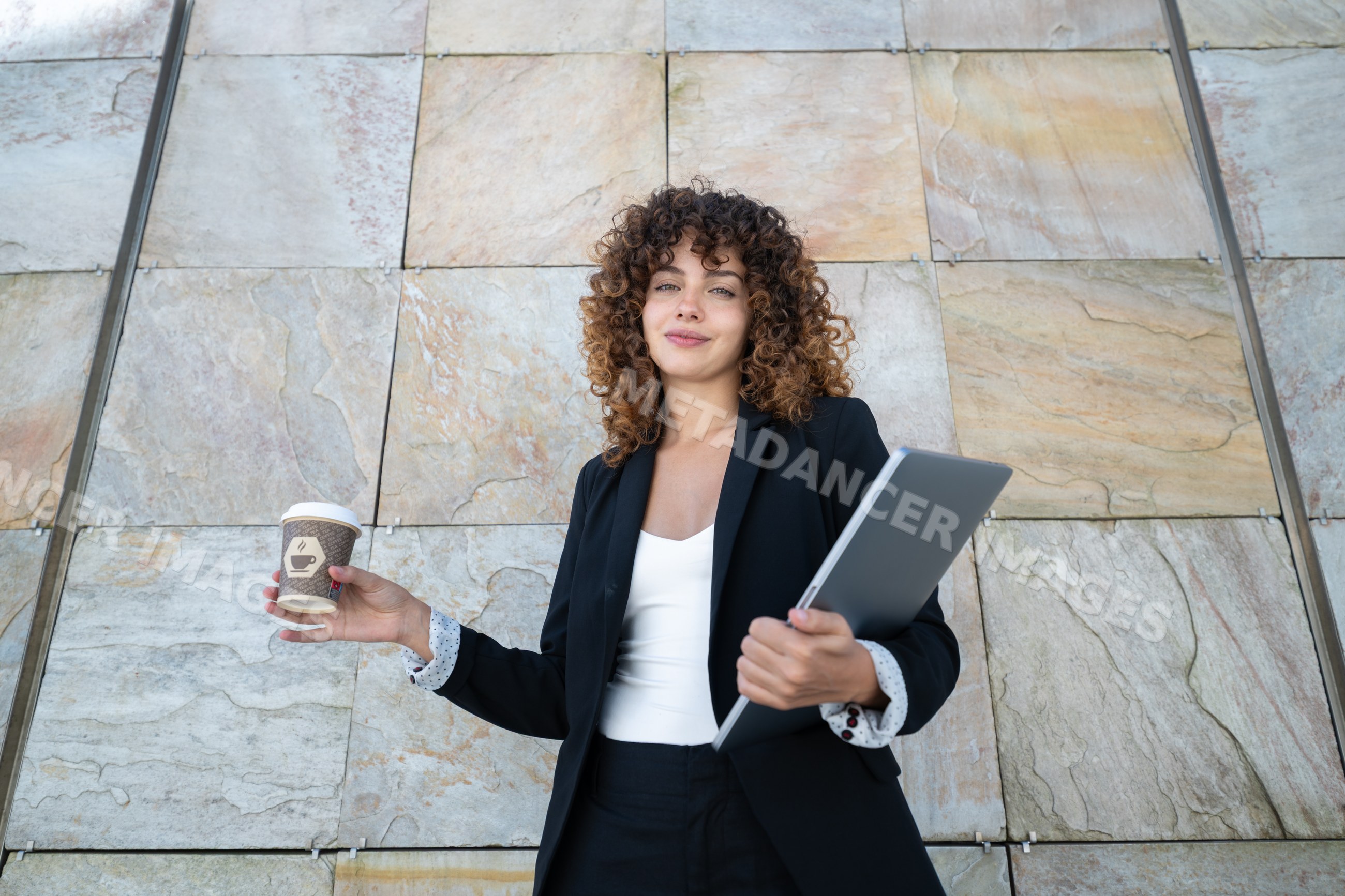 White woman holding coffee cup and laptop outdoors