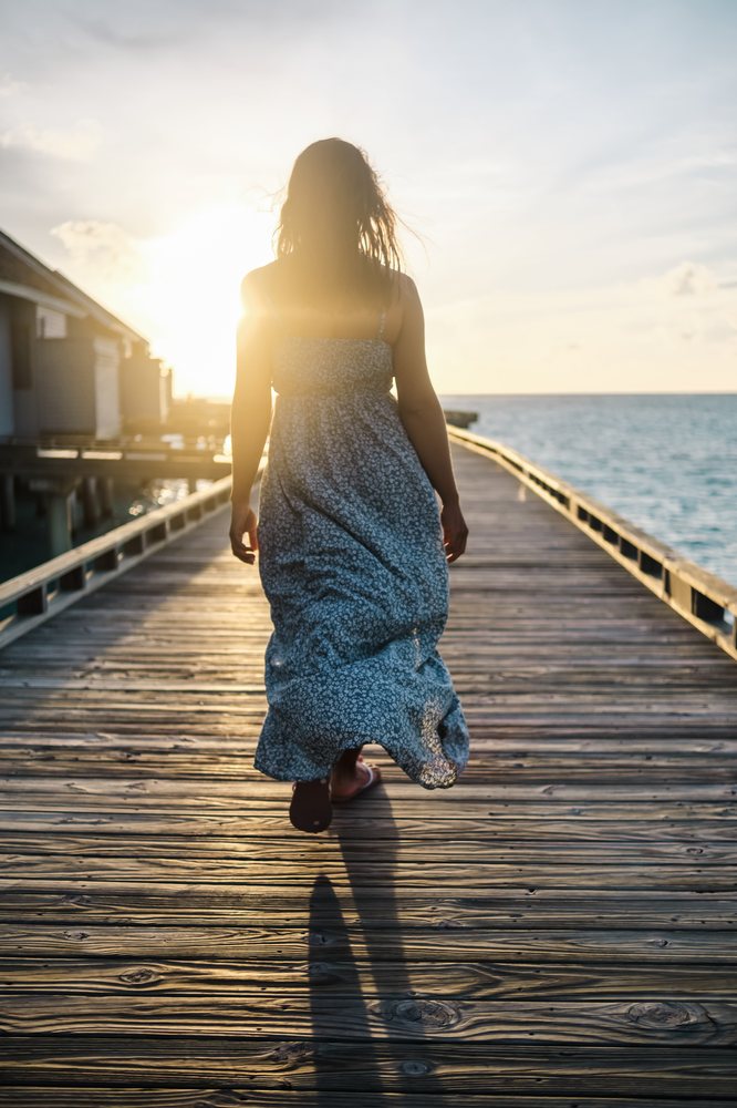 A white woman walks on a wooden pier over the ocean