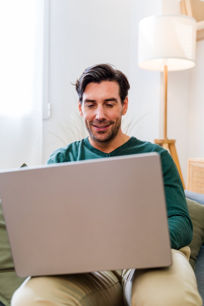 White man sitting on couch using laptop indoors