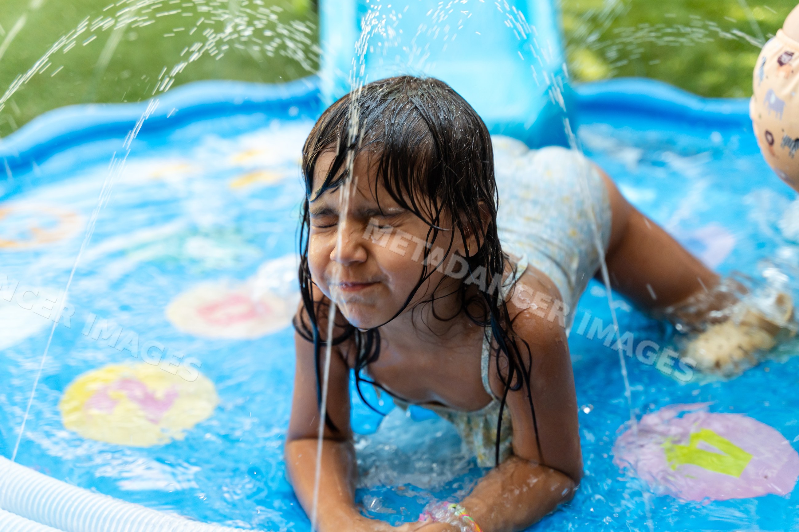 A young white girl plays and splashes in an inflatable paddling pool