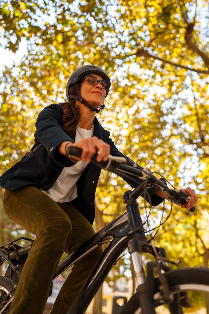 Hispanic woman riding bike outdoors under autumn trees in a park