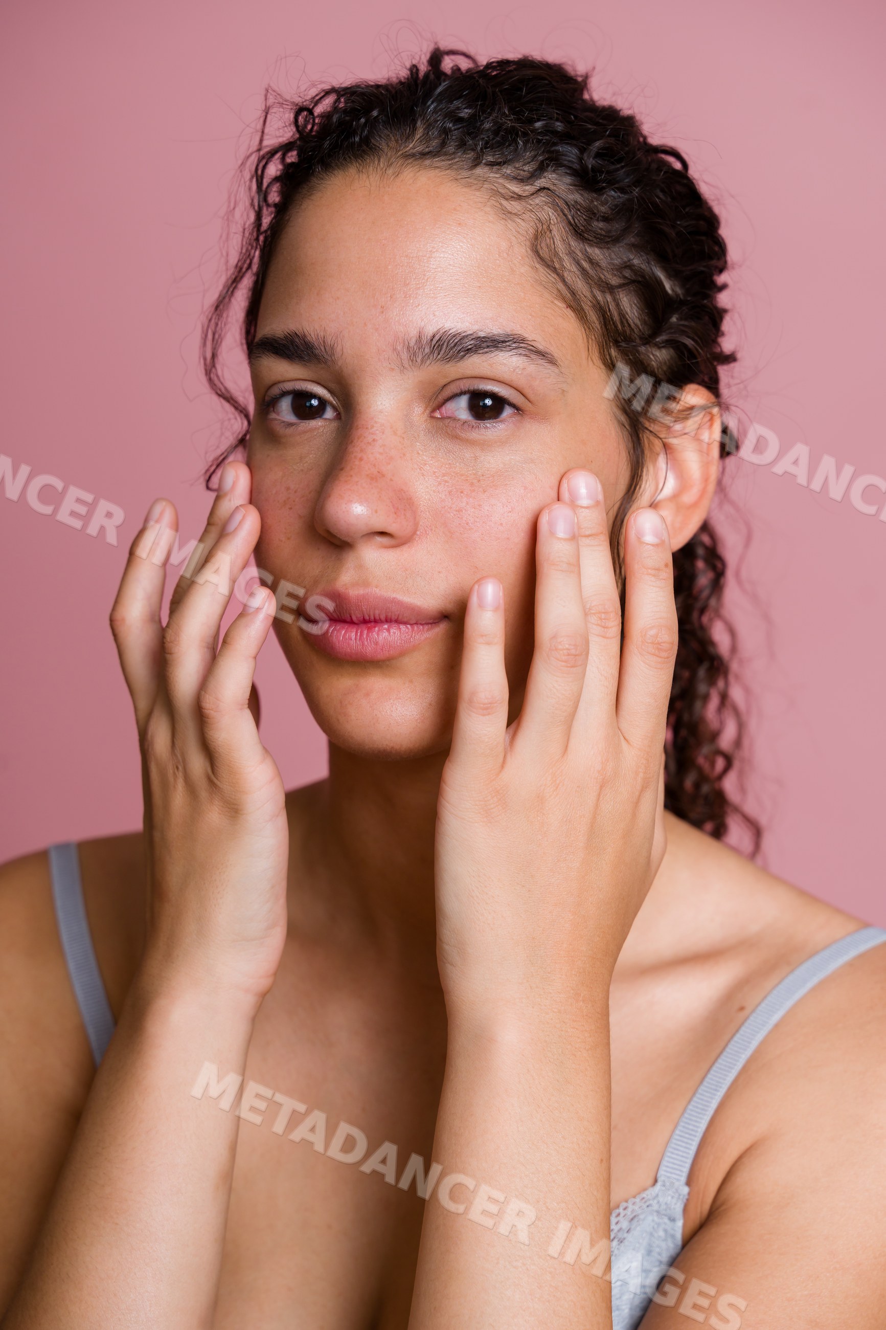 Hispanic woman touching her face with natural curly hair against pink