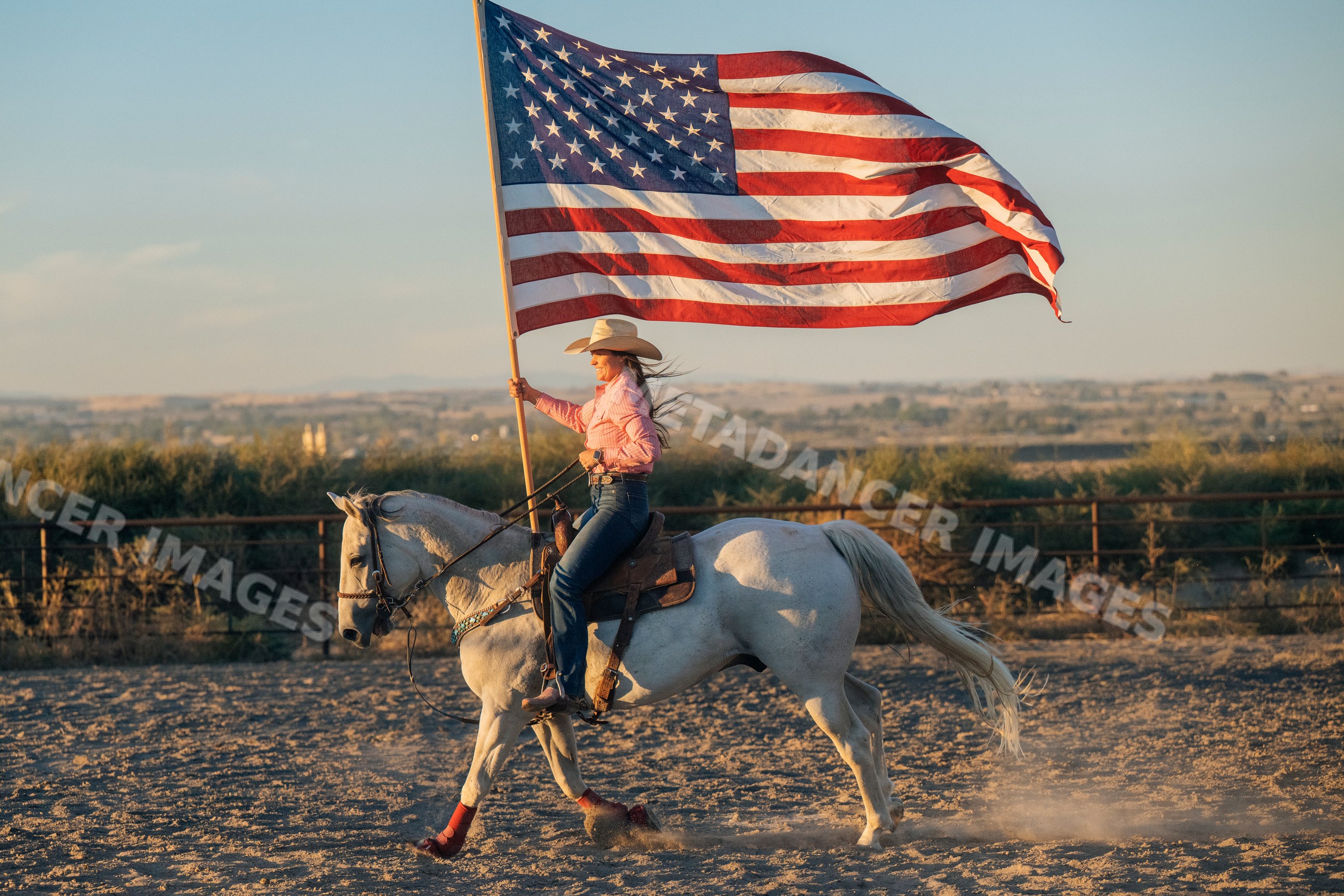 White woman riding a horse holding large american flag outdoors