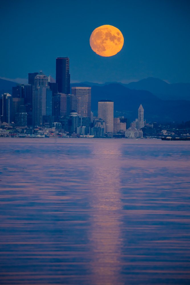 Full moon rising over Seattle city skyline with water reflection
