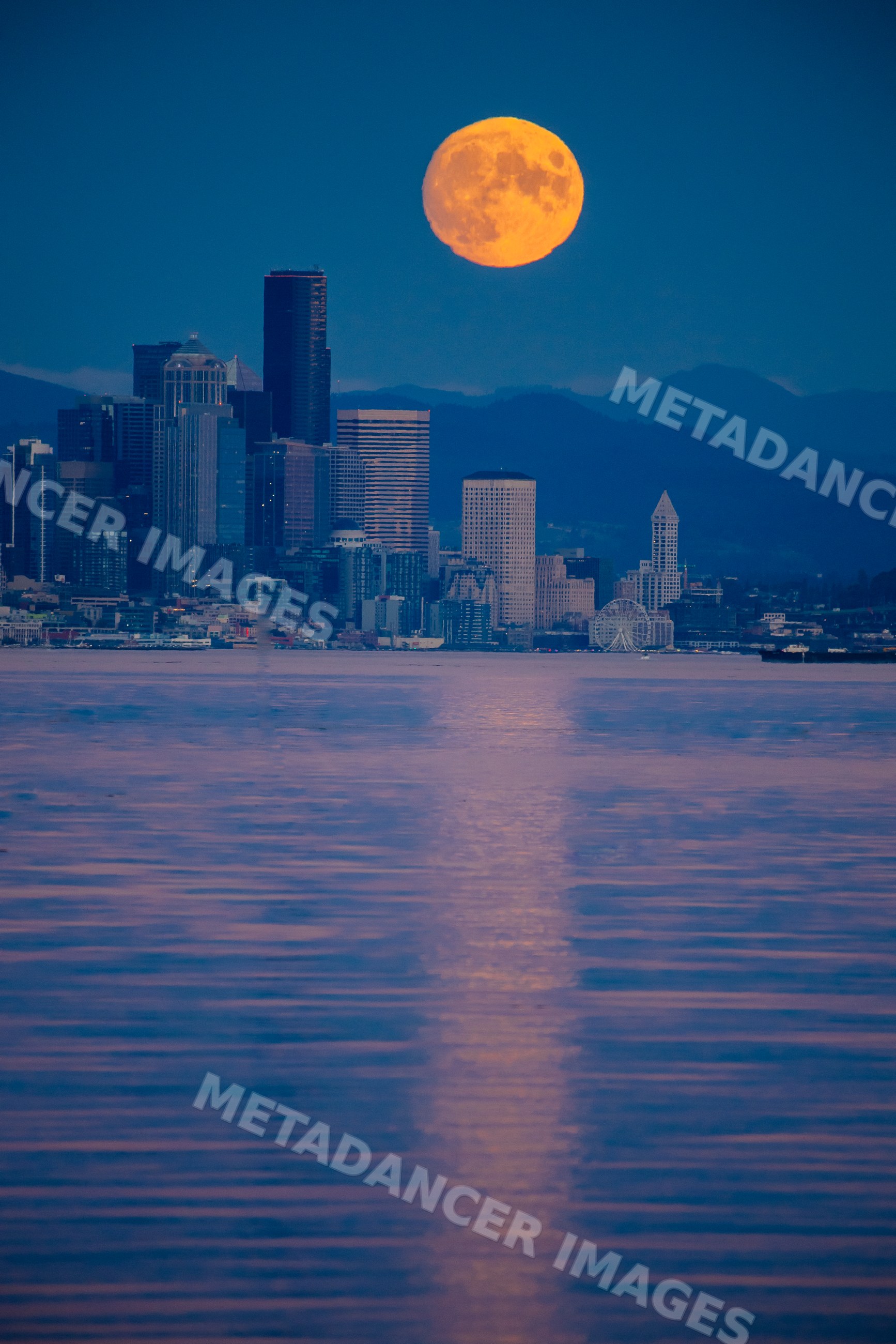 Full moon rising over Seattle city skyline with water reflection
