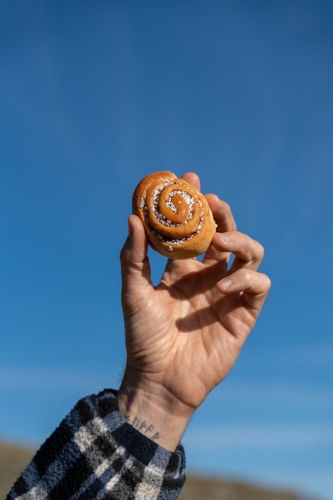 Cinnamon roll held against blue sky outdoors
