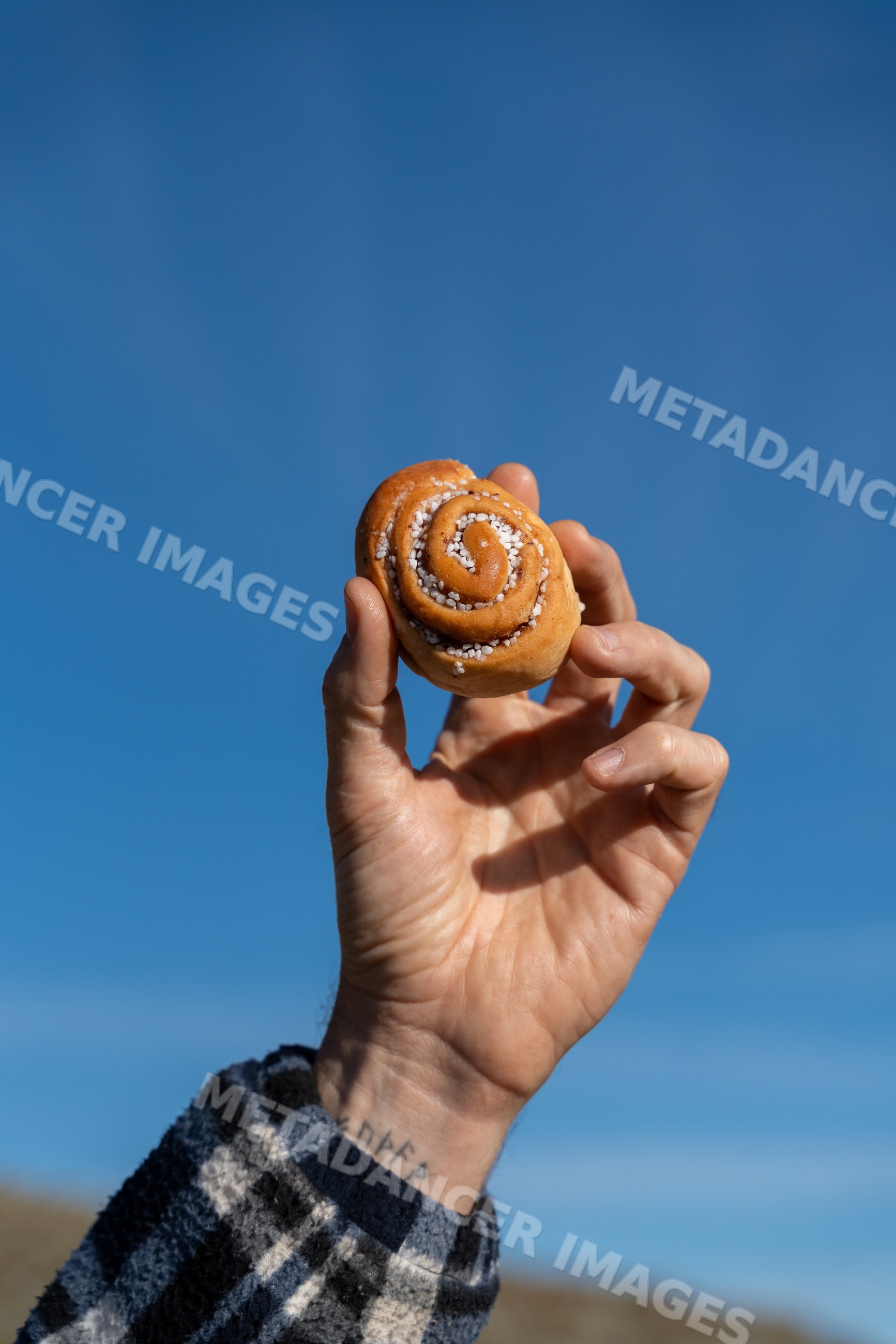 Cinnamon roll held against blue sky outdoors
