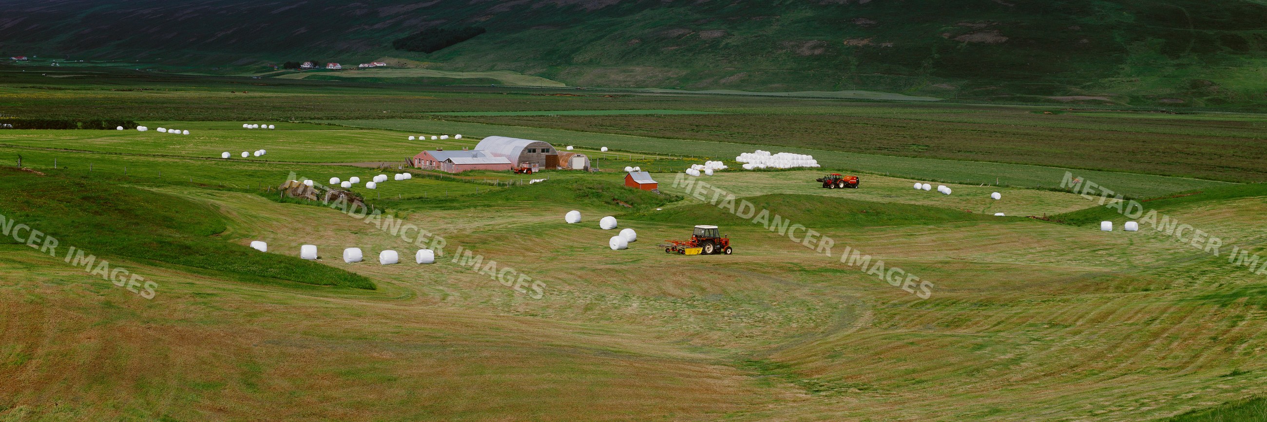 Farm landscape with hay bales and tractors working