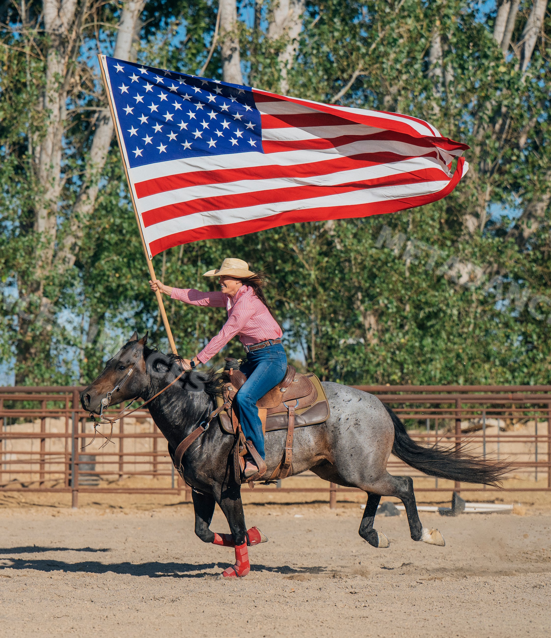 White woman riding horse waving american flag in outdoor arena