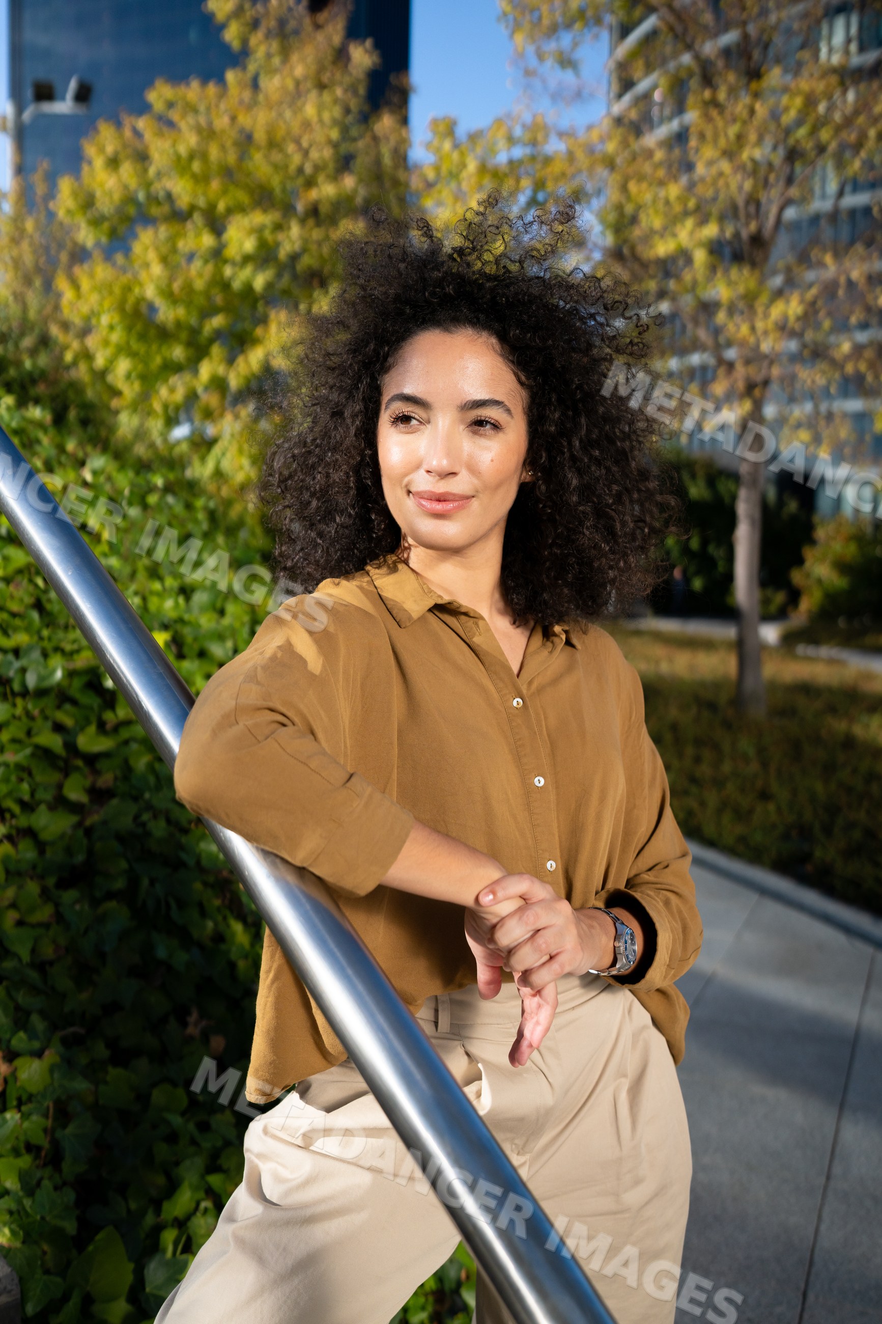 Woman leaning on handrail in urban park with curly dark hair