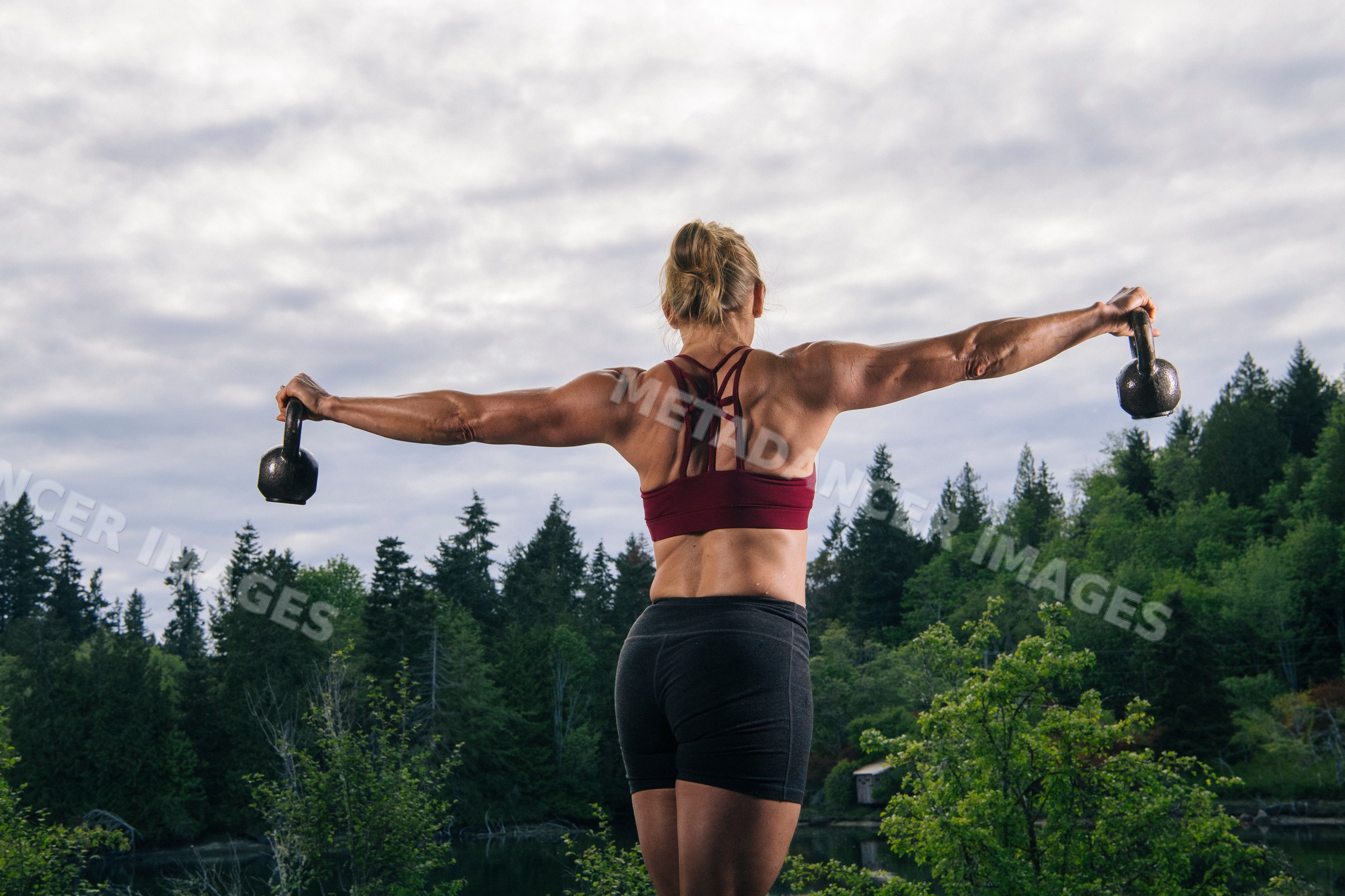 White woman lifting kettlebells outdoors by lake in natural setting