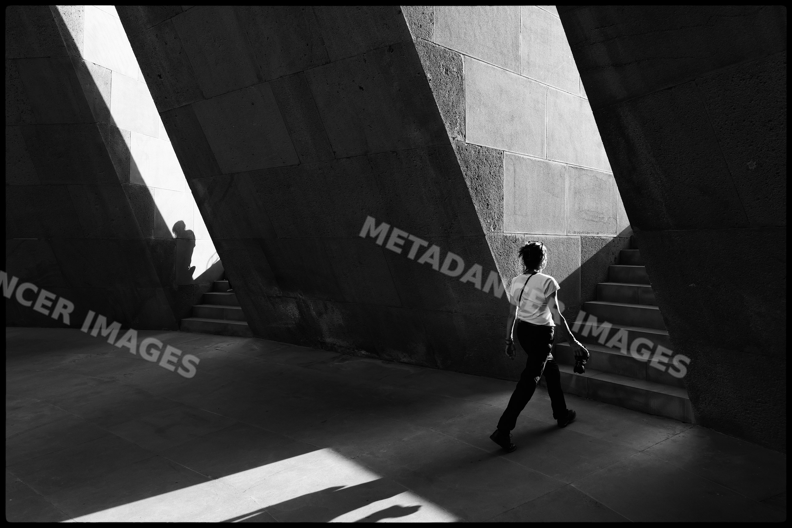 Person walking near stairs casting shadows at tsitsernakaberd memorial