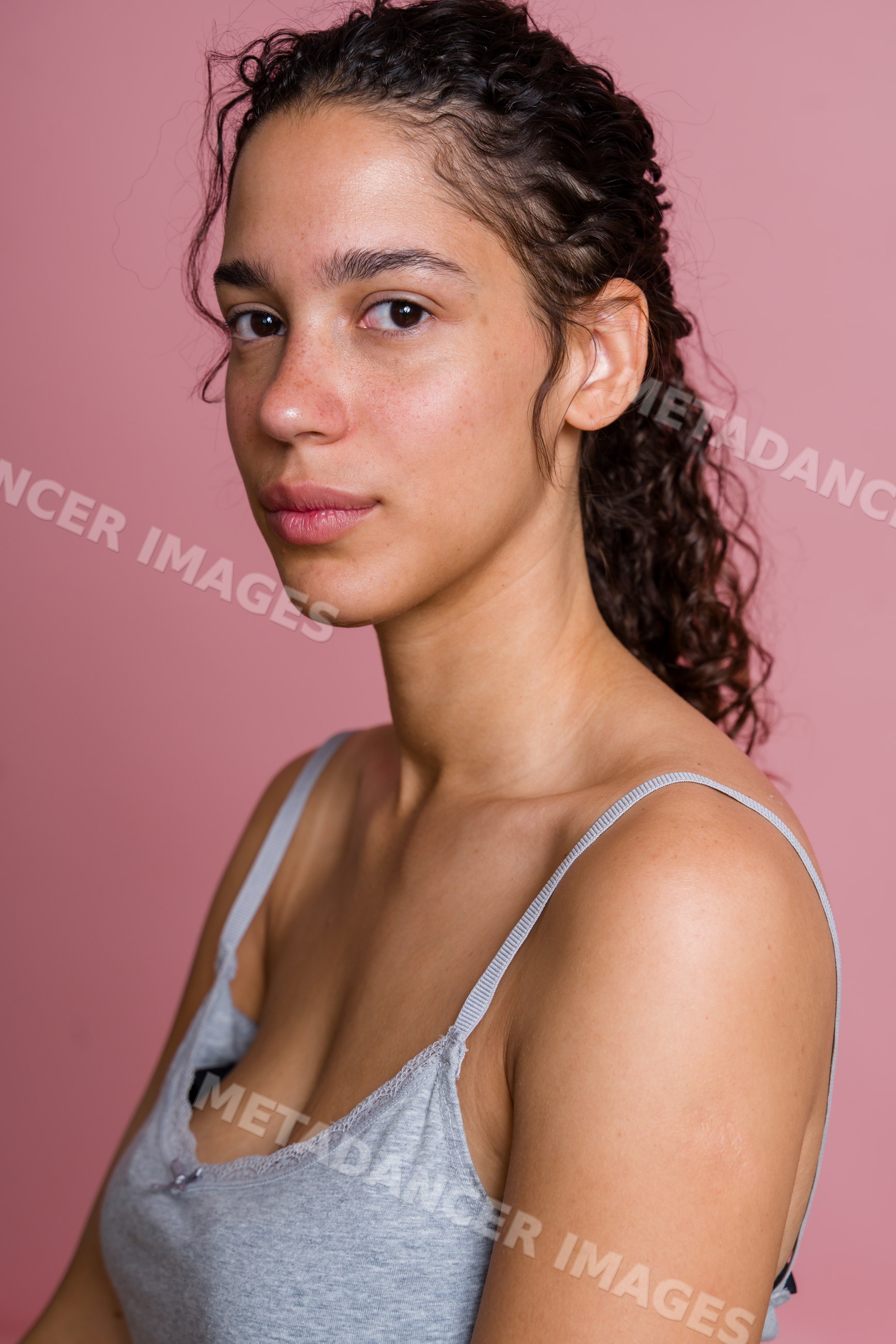 Portrait of young Hispanic woman with curly hair on pink background
