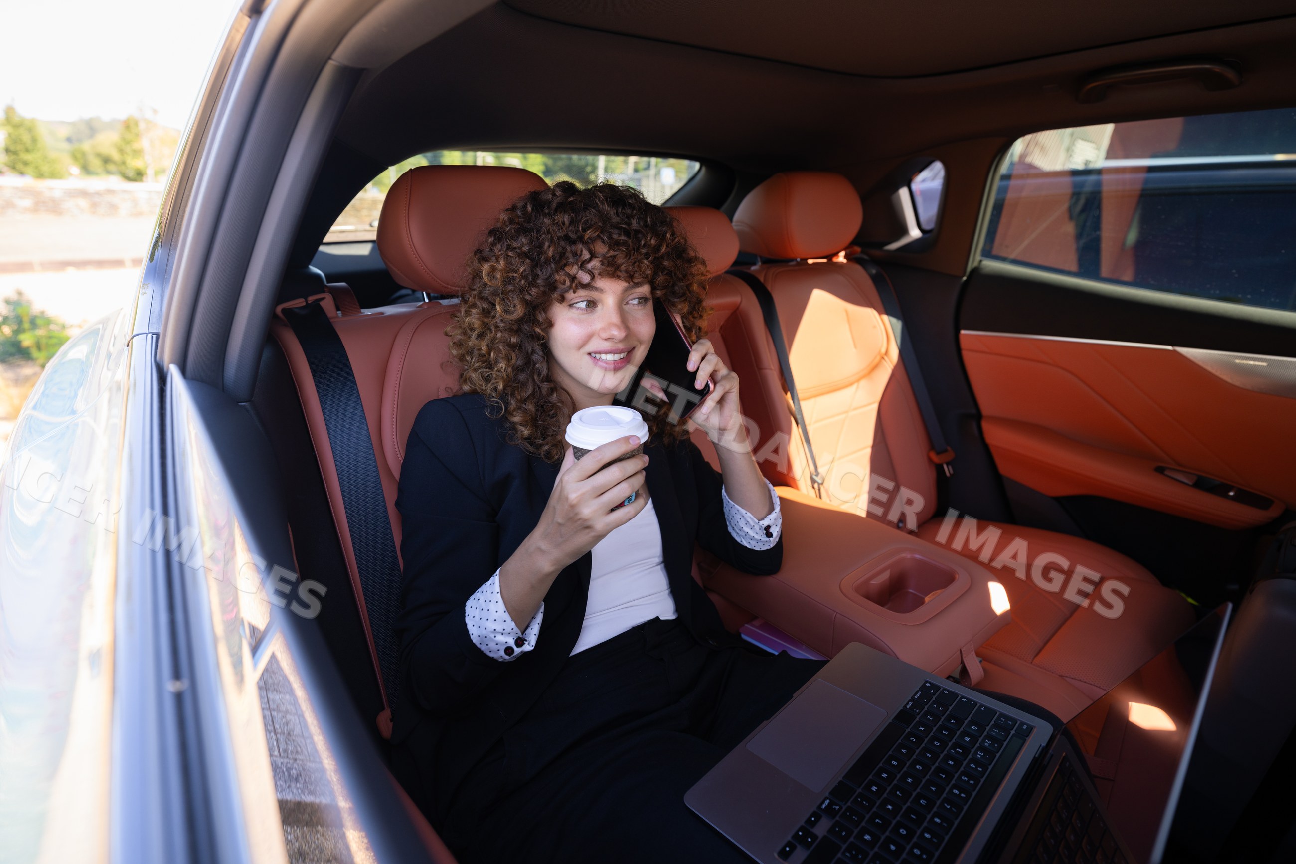 Businesswoman working remotely with laptop and coffee in car interior