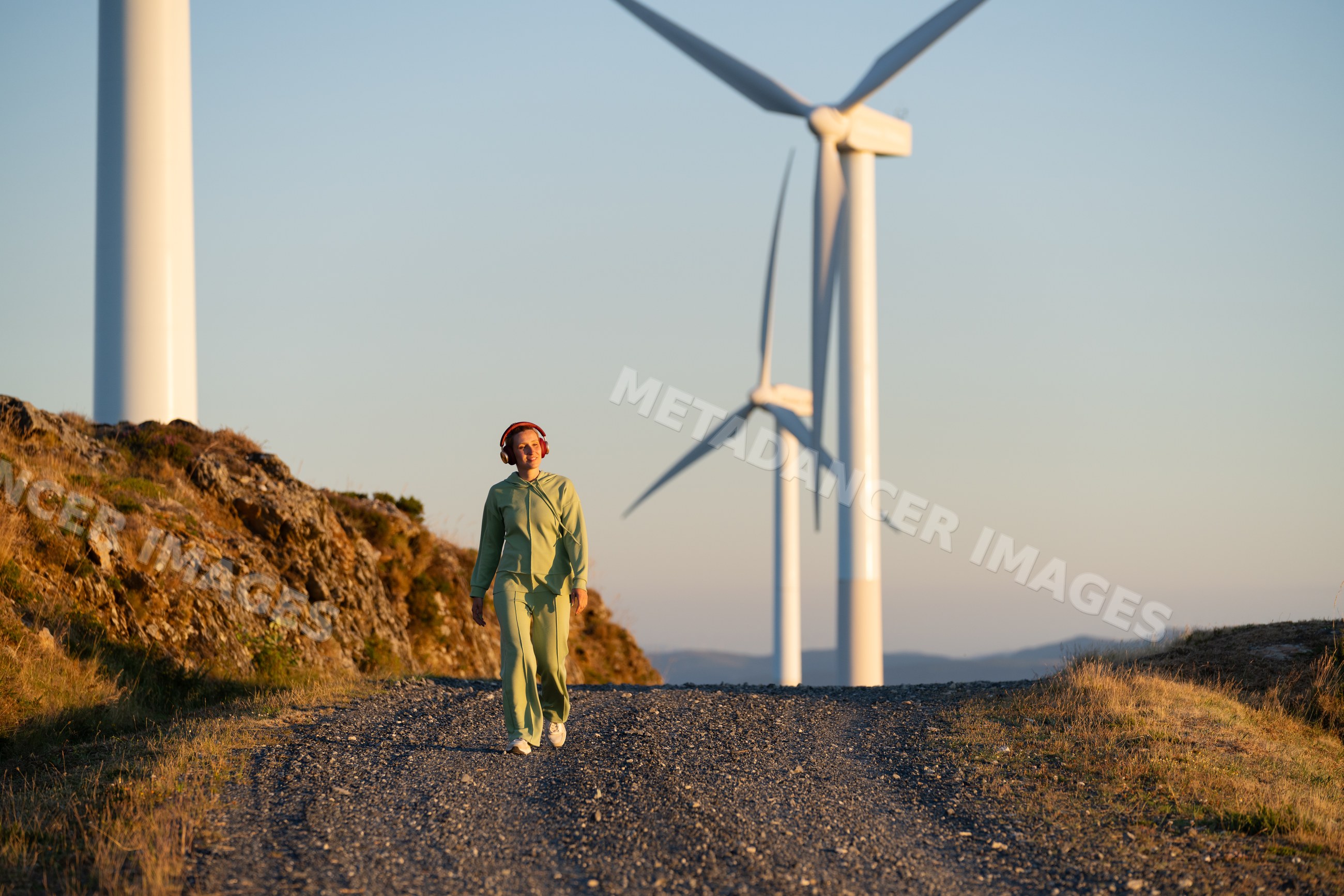 A white woman in a green tracksuit walks near wind turbines in Galicia