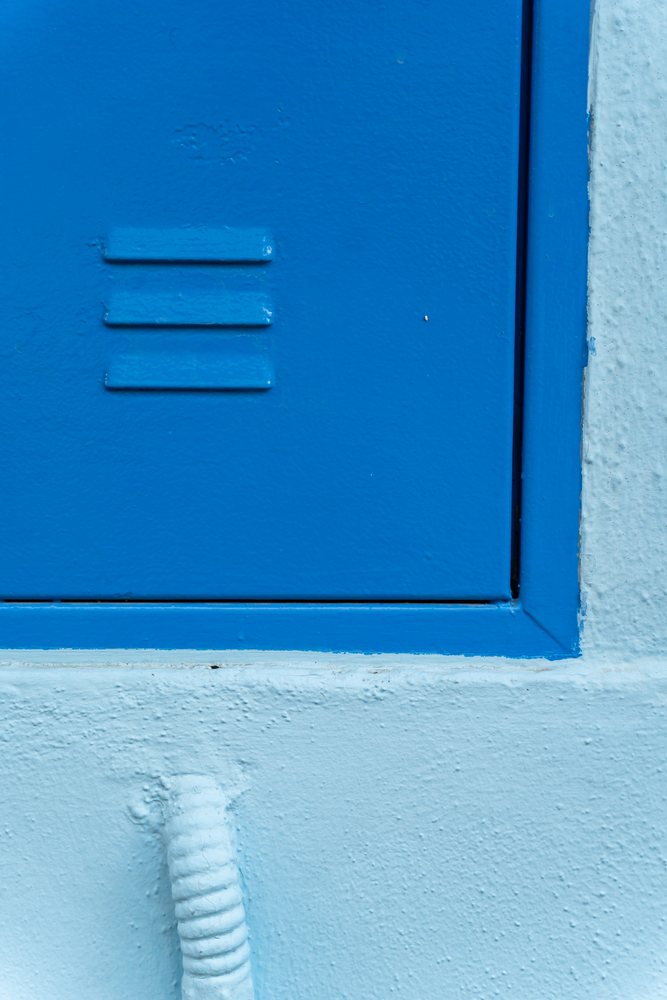 Blue metal door with ventilation slits and textured blue wall