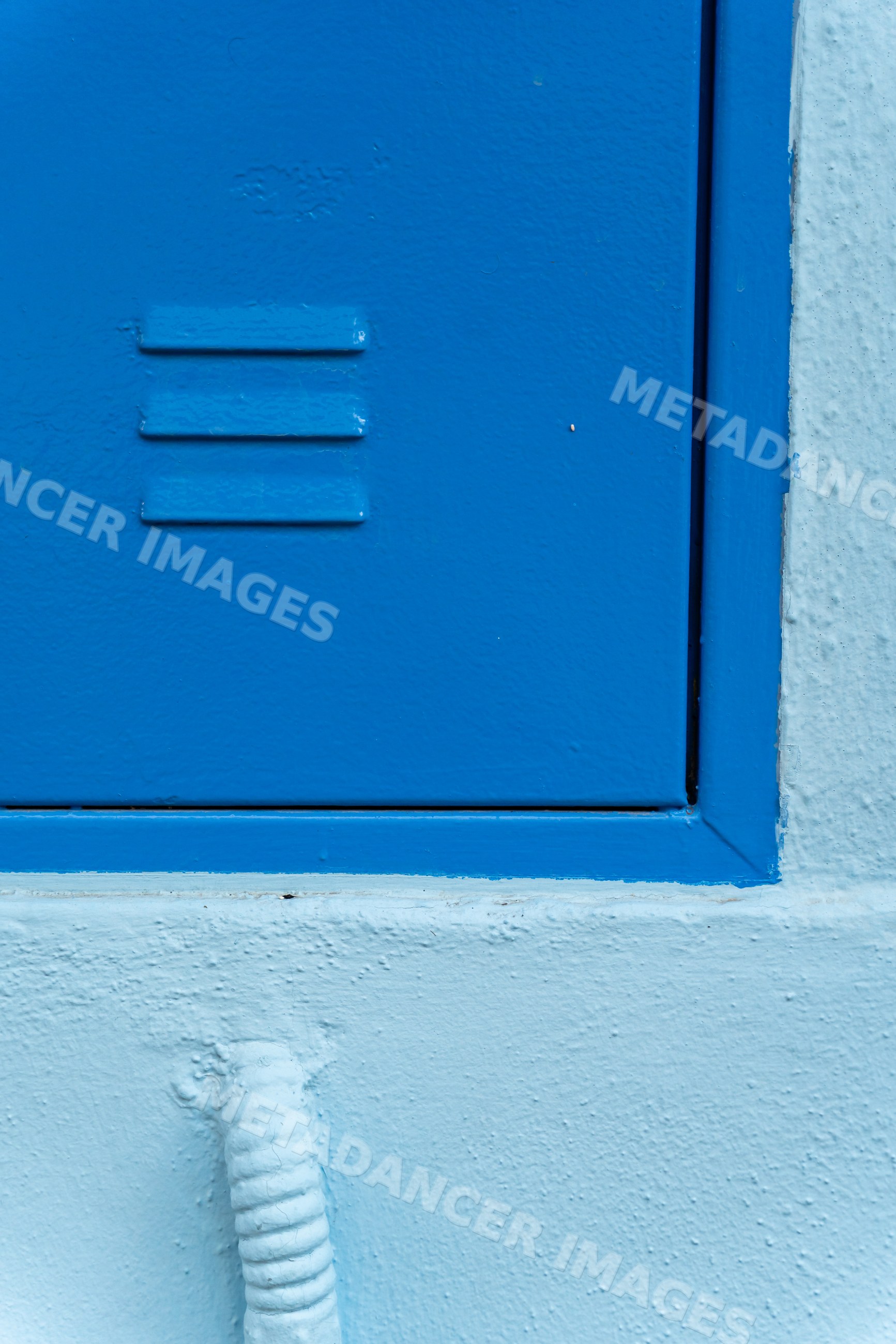 Blue metal door with ventilation slits and textured blue wall