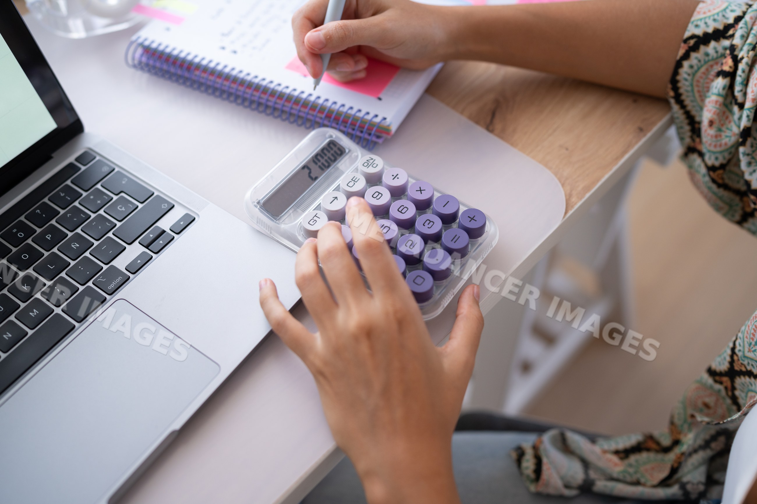 Hands calculating and taking notes beside laptop